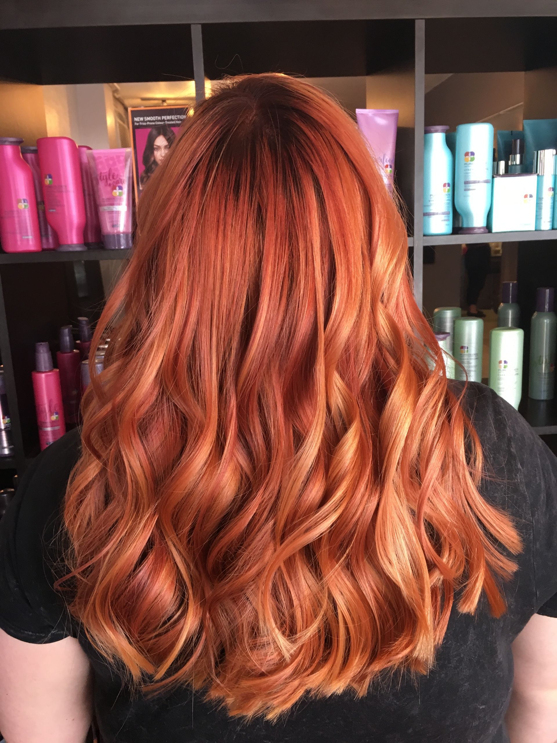 A person from behind displays long, wavy, vibrant copper-red hair in a hair salon.