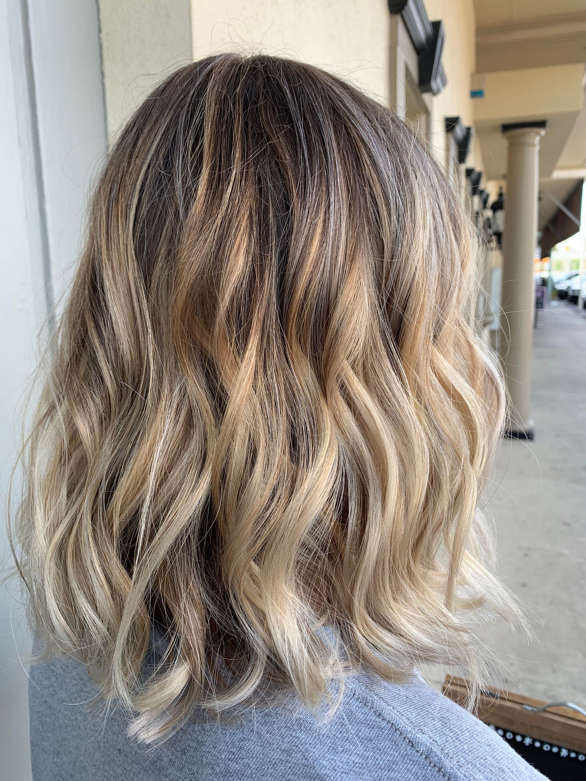 Back view of wavy, textured hair with a blonde ombre color transition, shown in an outdoor setting.