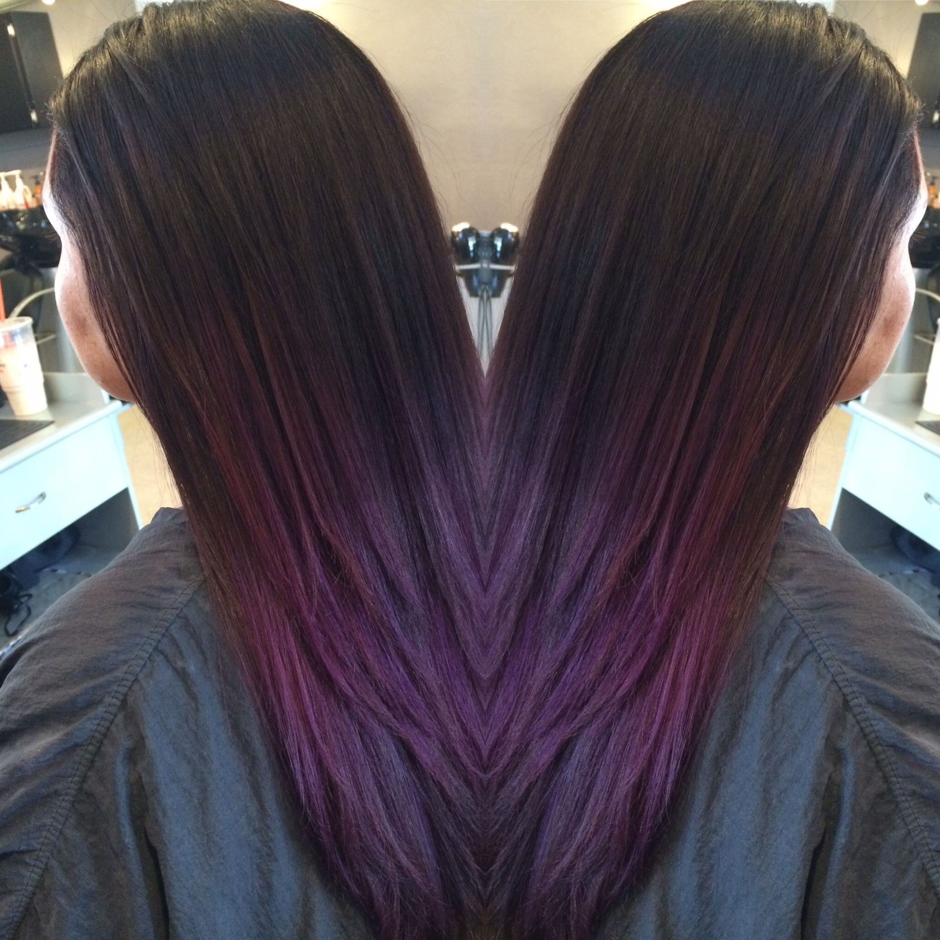 Long dark hair styled with a deep purple ombre fade, shown from the back in a mirrored composition in a salon setting.