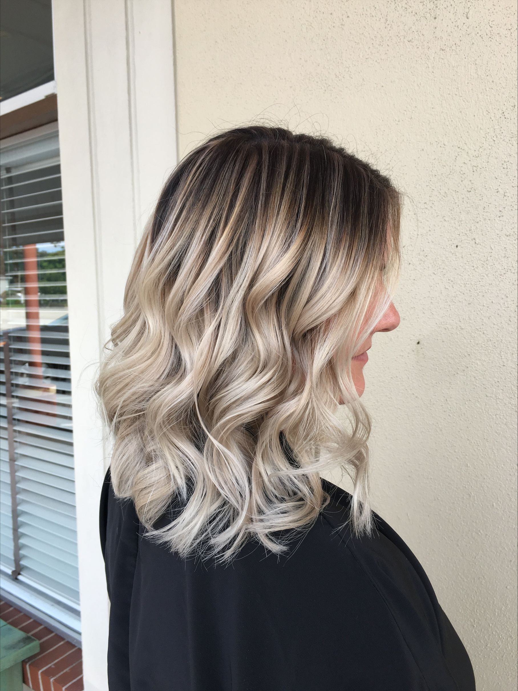 Back view of wavy, textured hair with a blonde ombre color transition, shown in an outdoor setting.