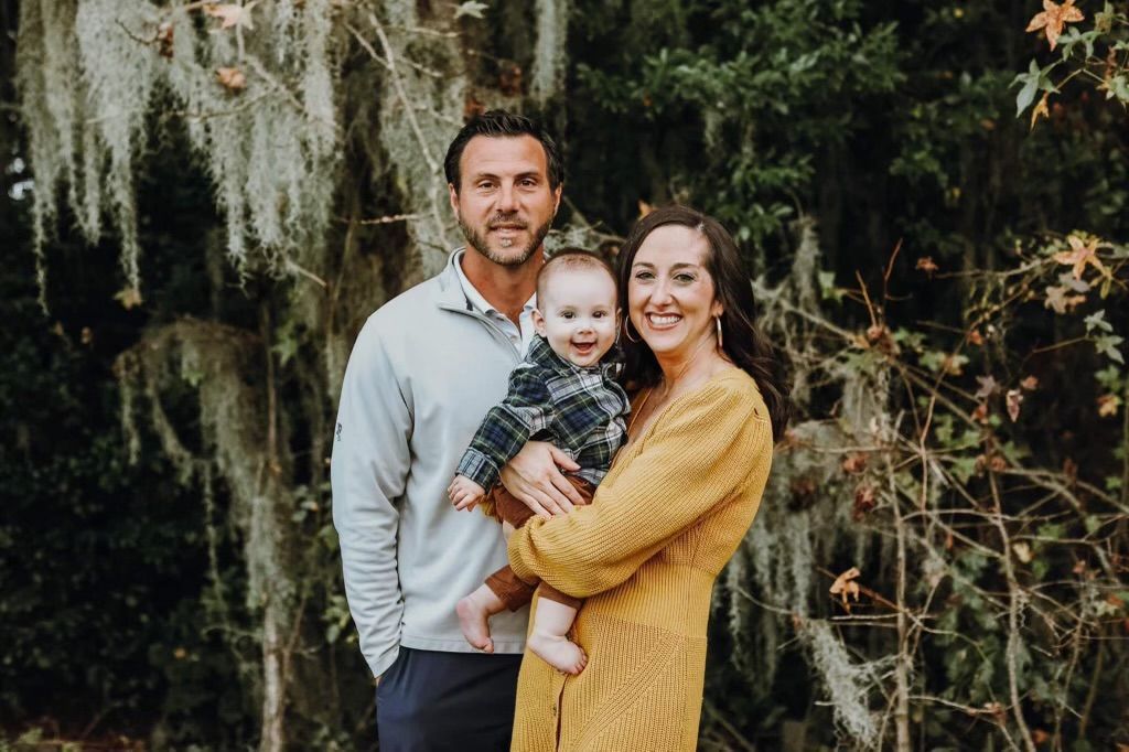 A man and woman are holding a baby in front of a tree.