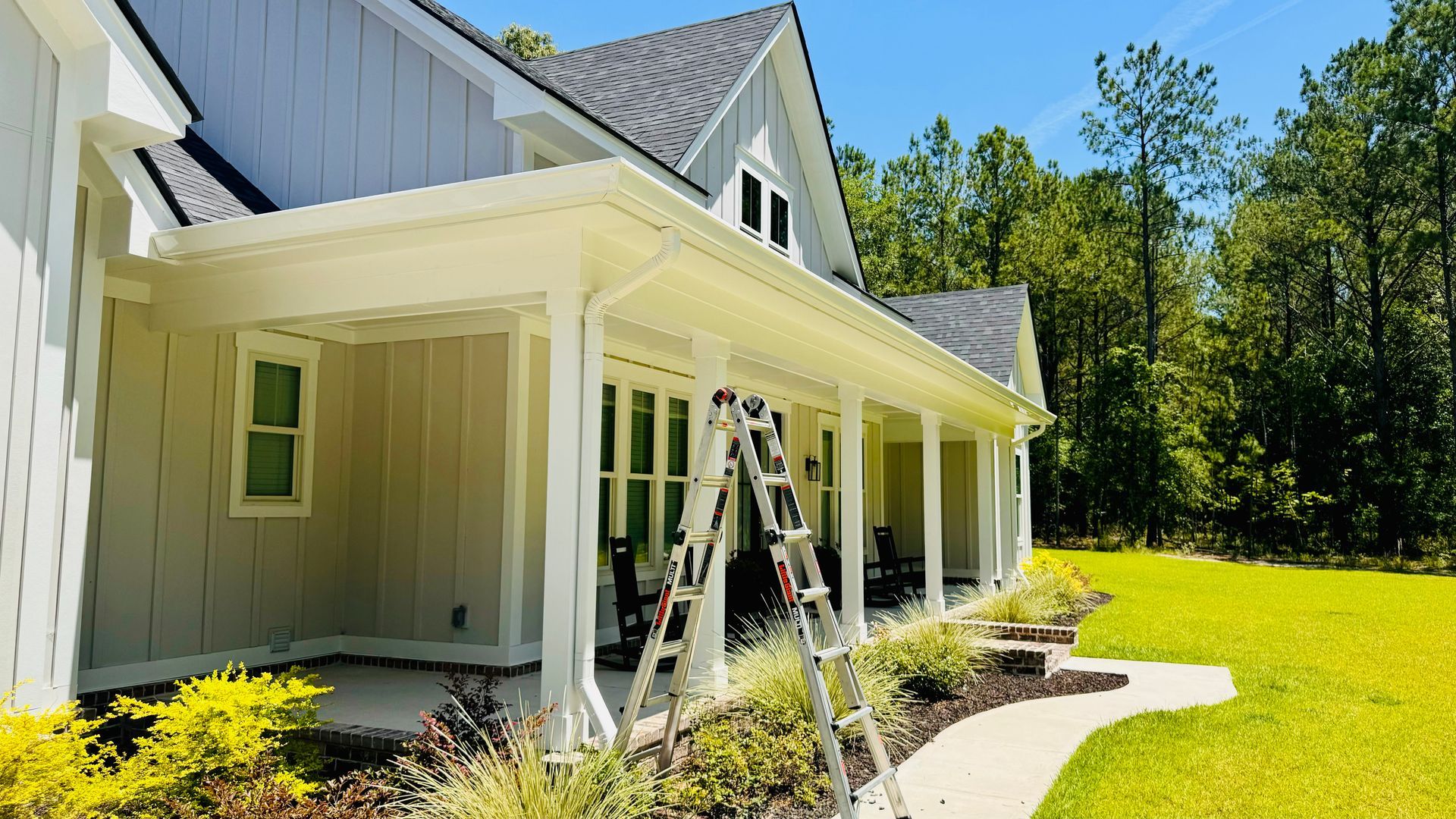 A white house with a porch and a ladder in front of it.