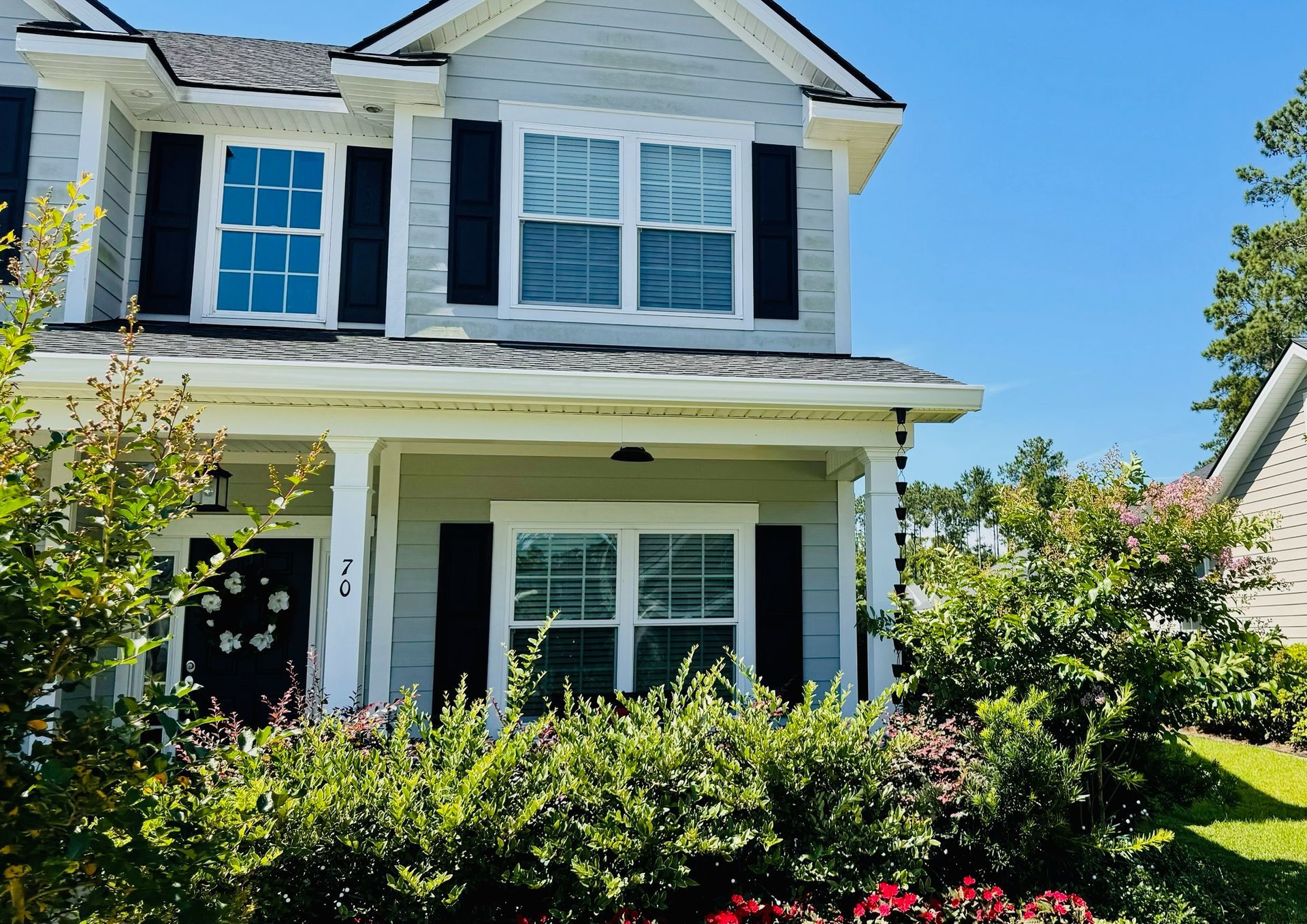 A white house with black shutters and flowers in front of it