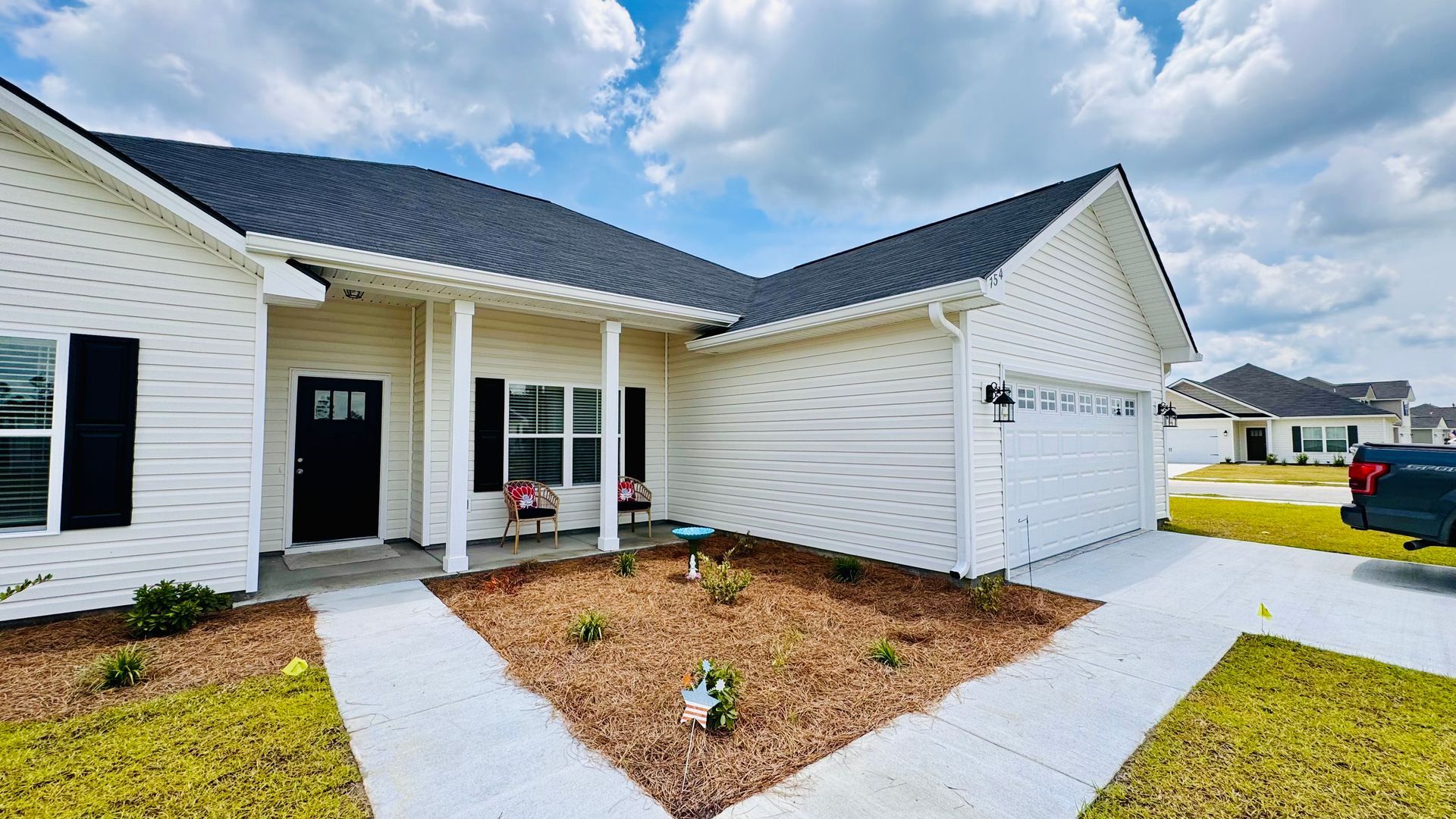 A white house with a black roof and a truck parked in front of it.
