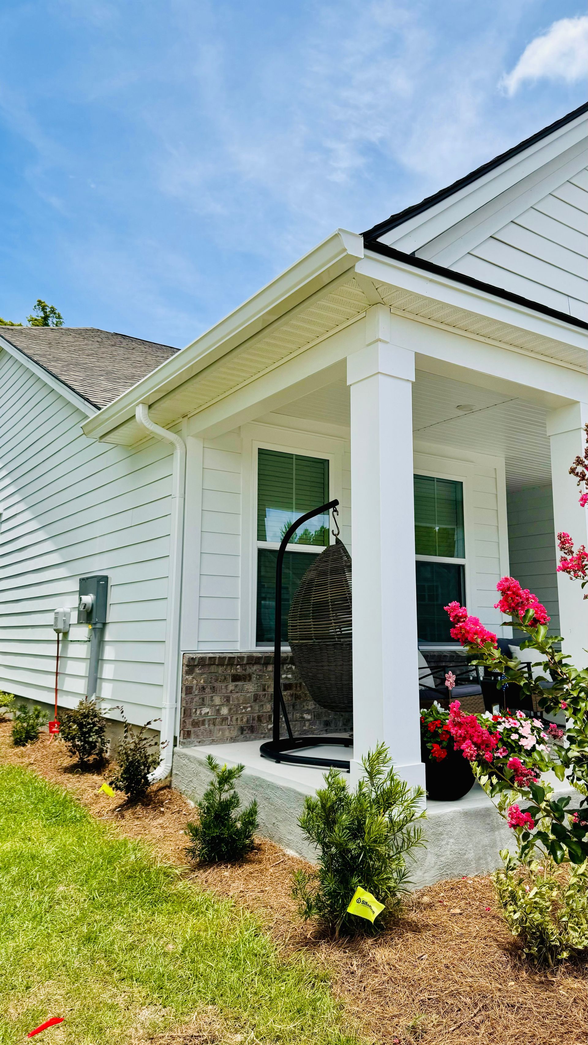 A white house with a porch and flowers in front of it.