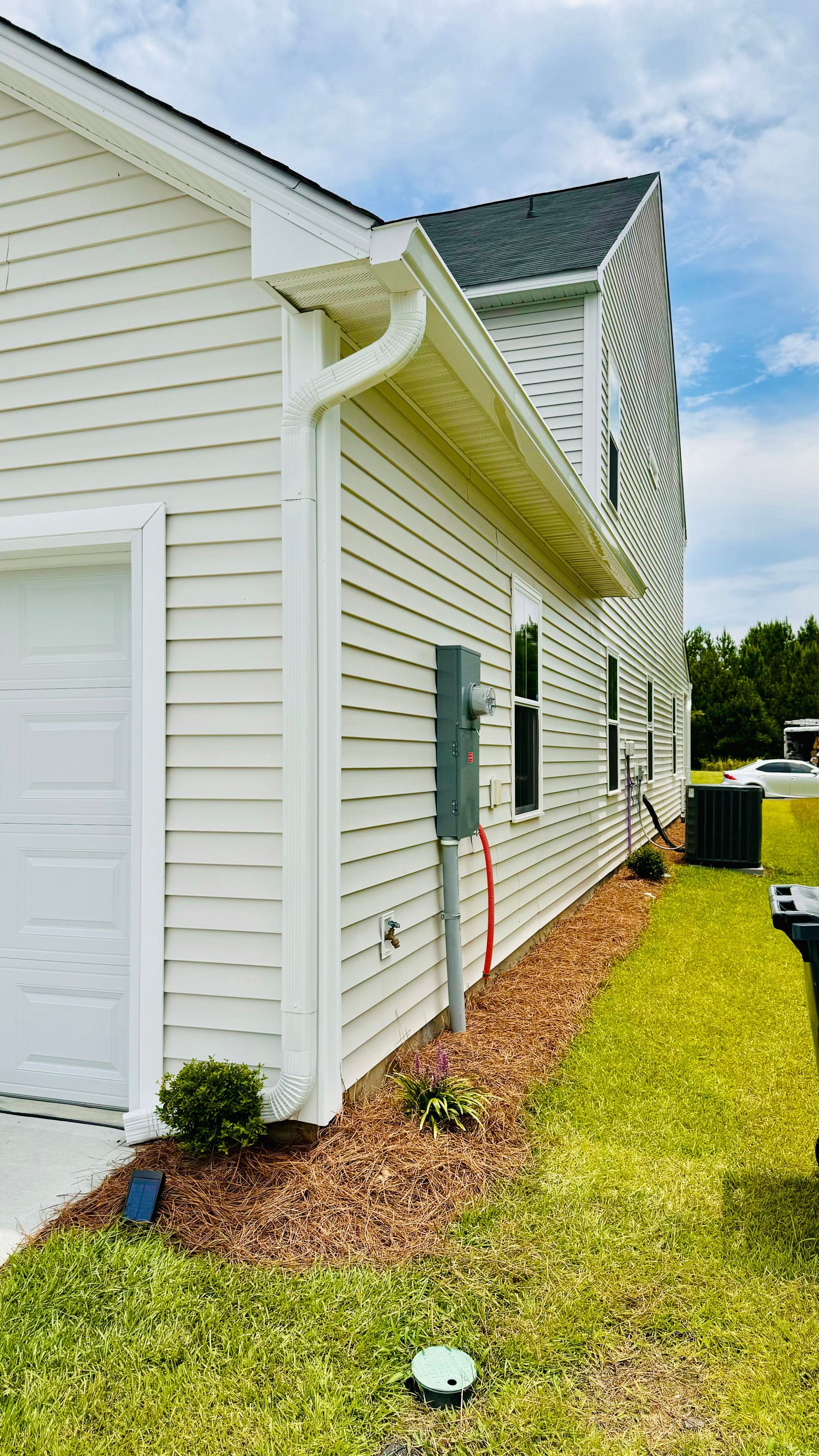 A white house with a garage and a gutter on the side of it.