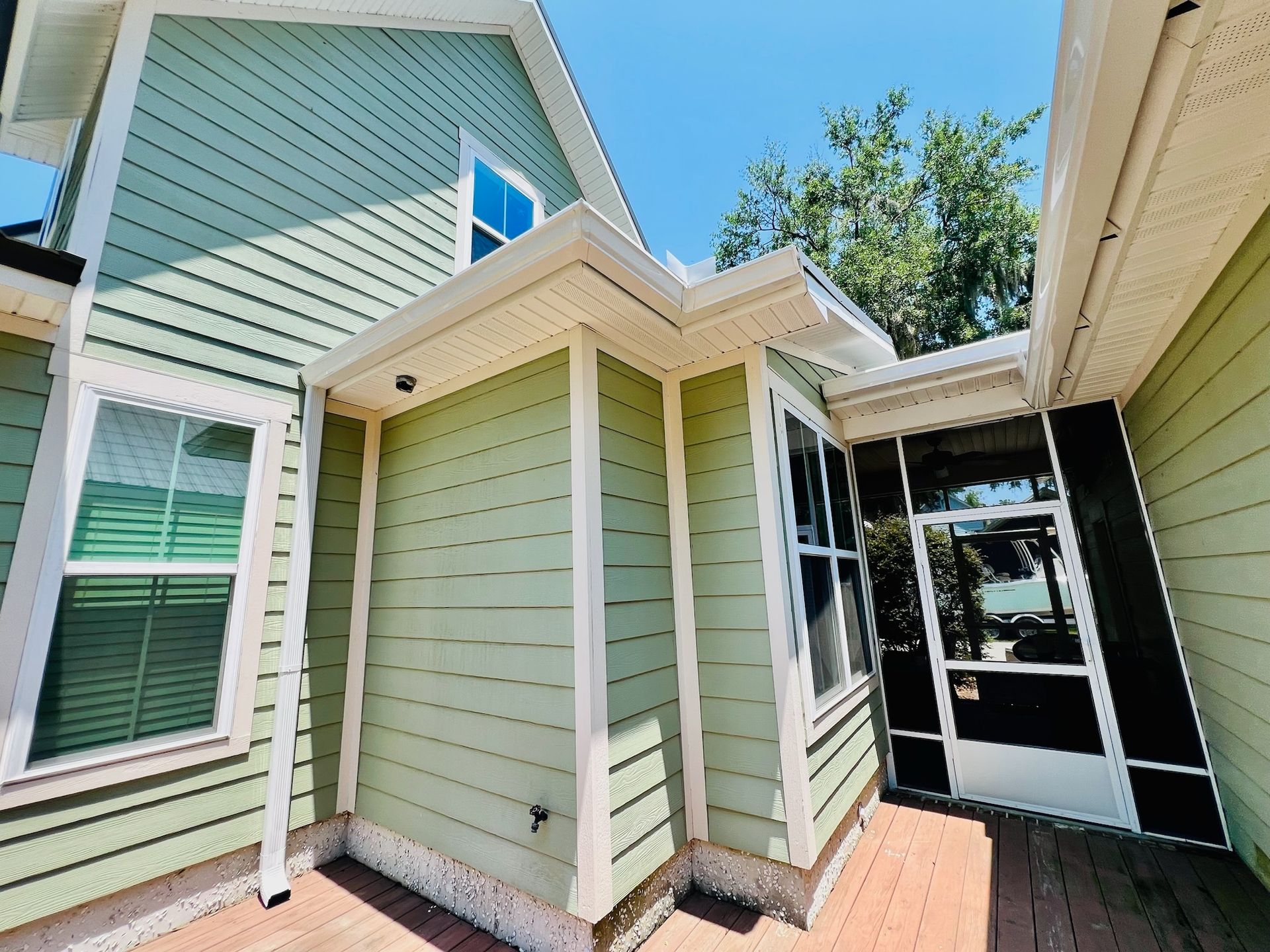 A green house with white trim and a screened in porch.
