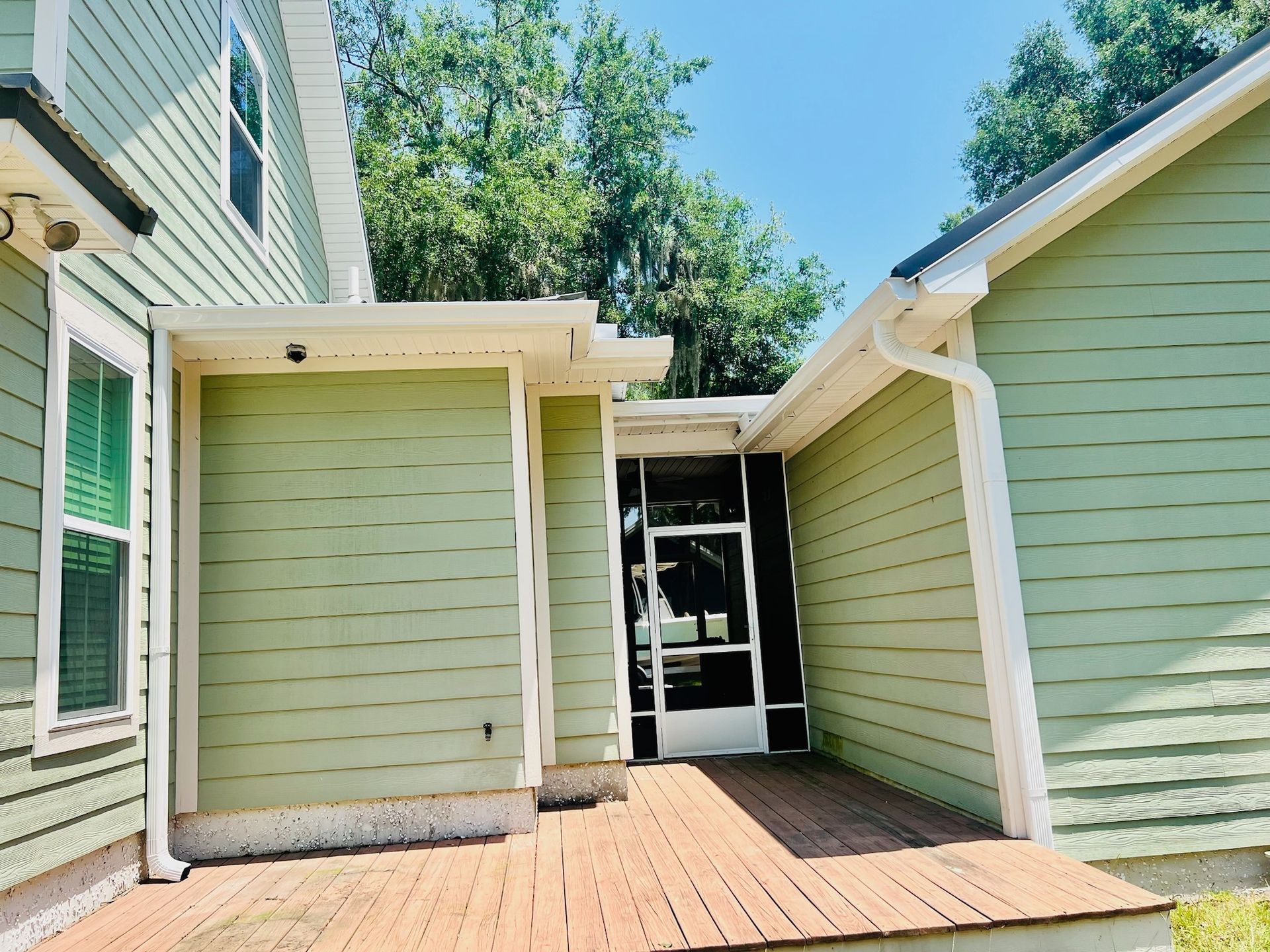 A green house with a screened in porch and a brick walkway