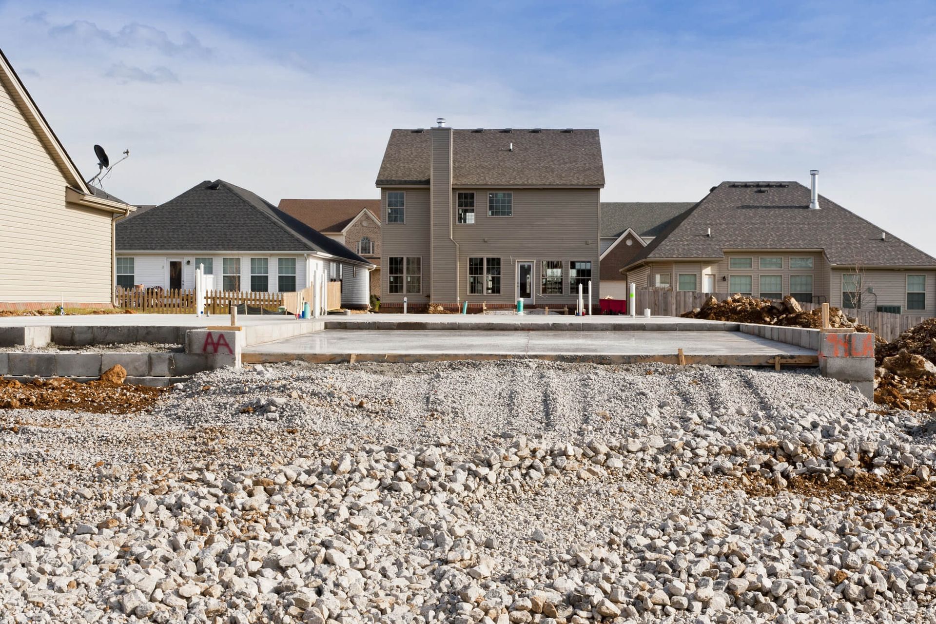 Construction site with a concrete patio base and houses in the background on a sunny day.