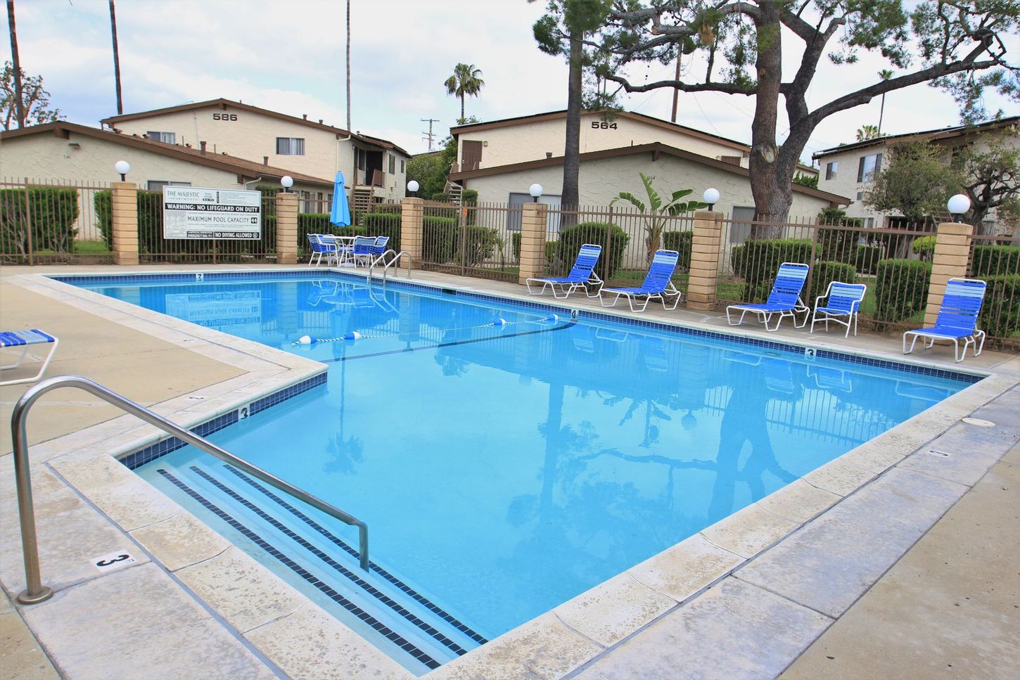 A large swimming pool is surrounded by chairs and buildings