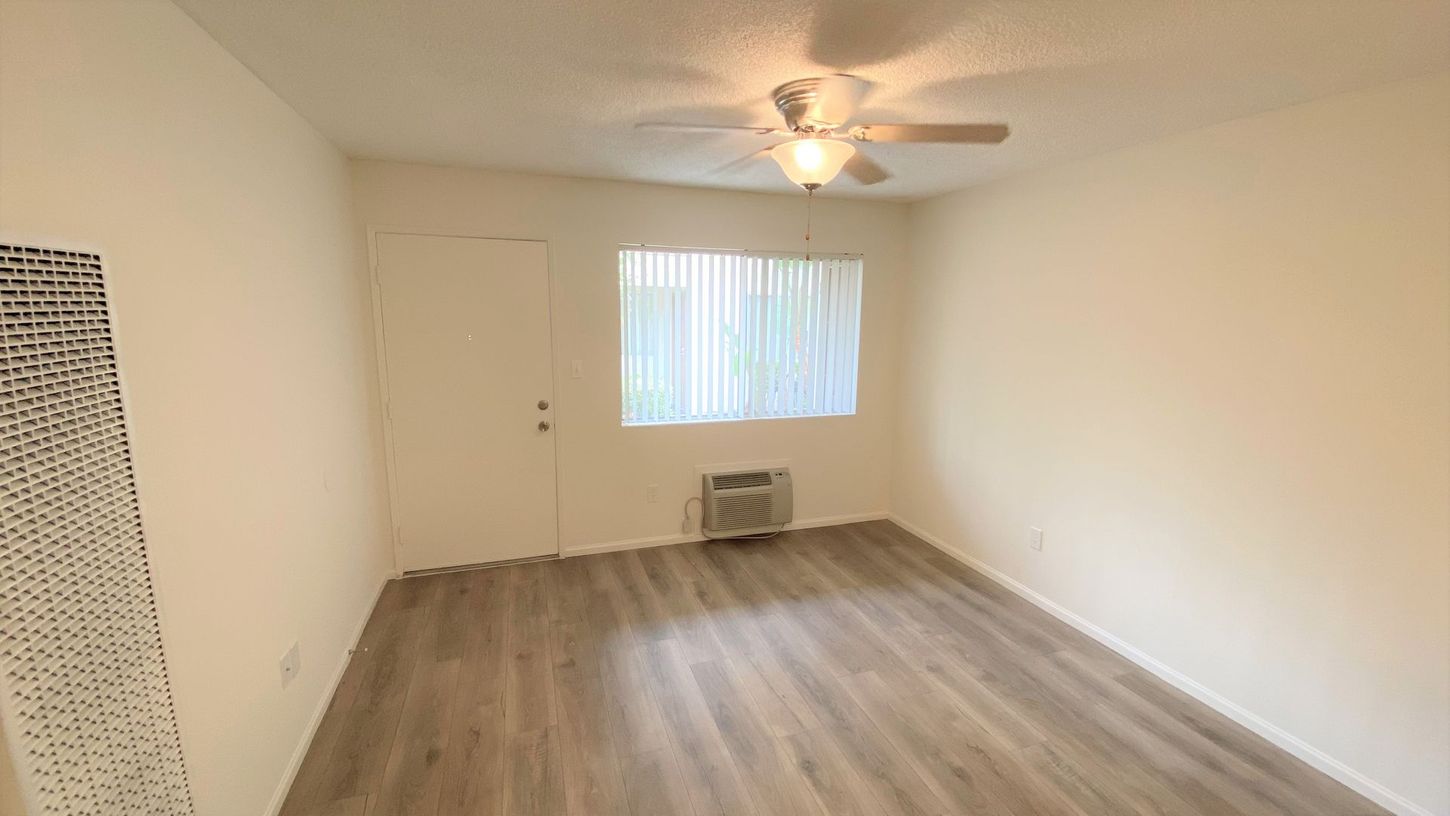 An empty living room with a ceiling fan and a window.