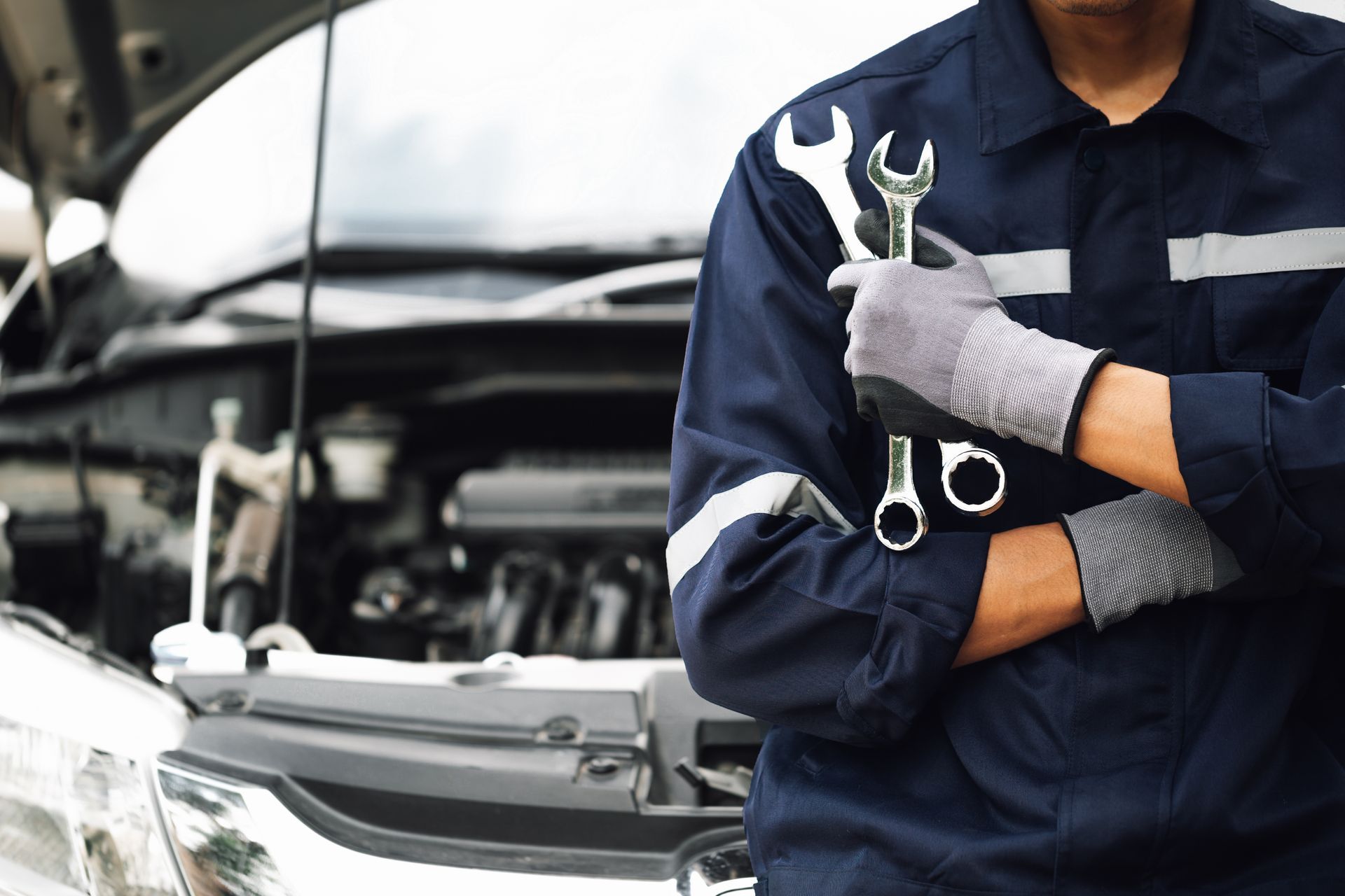 A mechanic is holding a wrench in front of a car with the hood open. | Halton Auto Service & Transmission