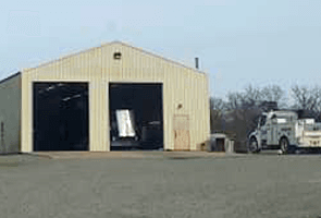 Beige metal building with open bays; service truck parked outside.