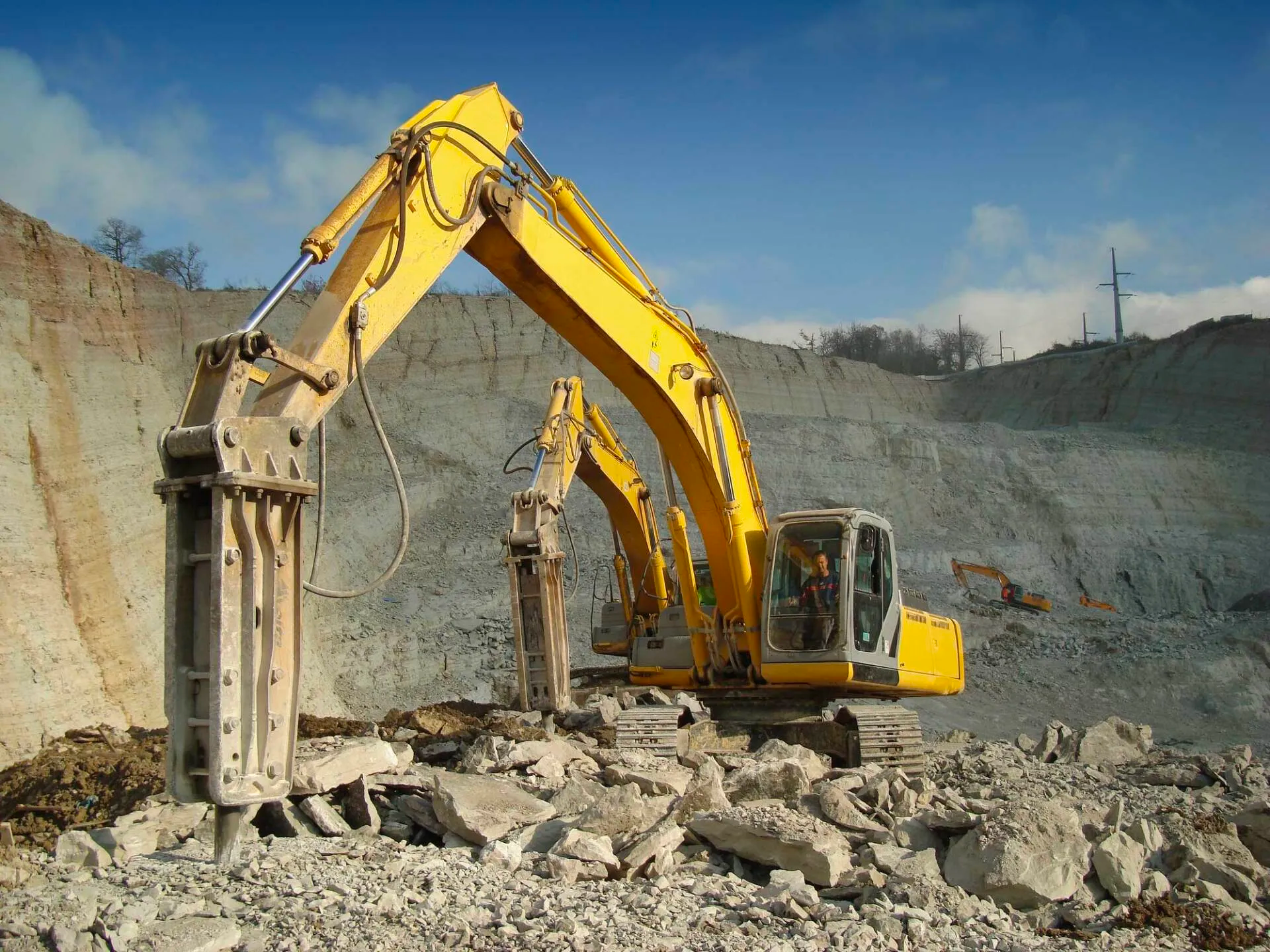 A yellow excavator is breaking rocks in a quarry