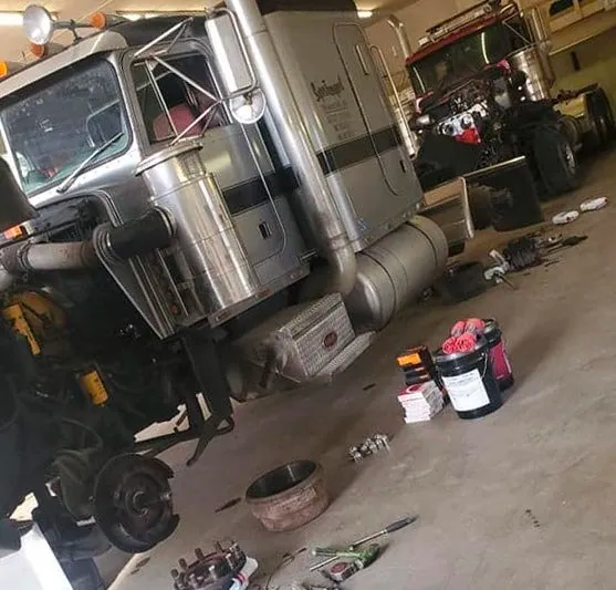 Semi-truck being worked on in a garage; parts and tools scattered on the floor.