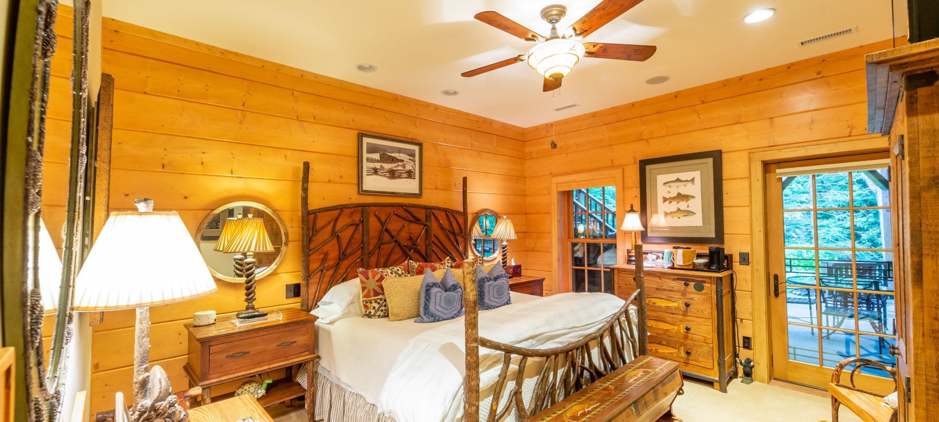 A bedroom in a log cabin with a king size bed , a ceiling fan , a mirror and a bench.