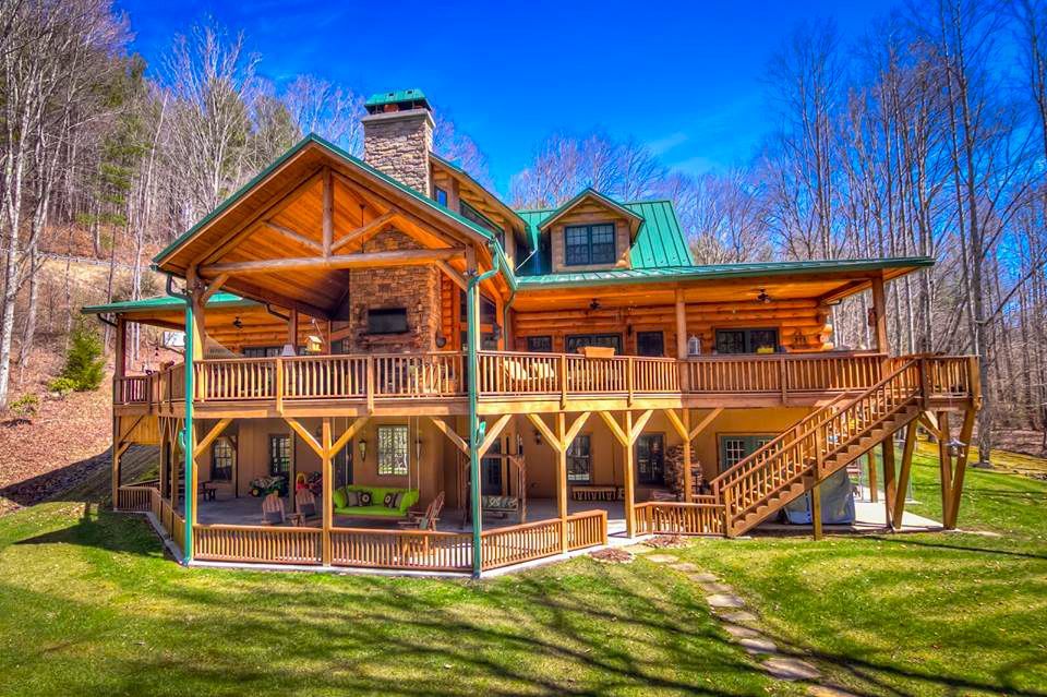 A large log cabin with a large deck in the middle of a forest.