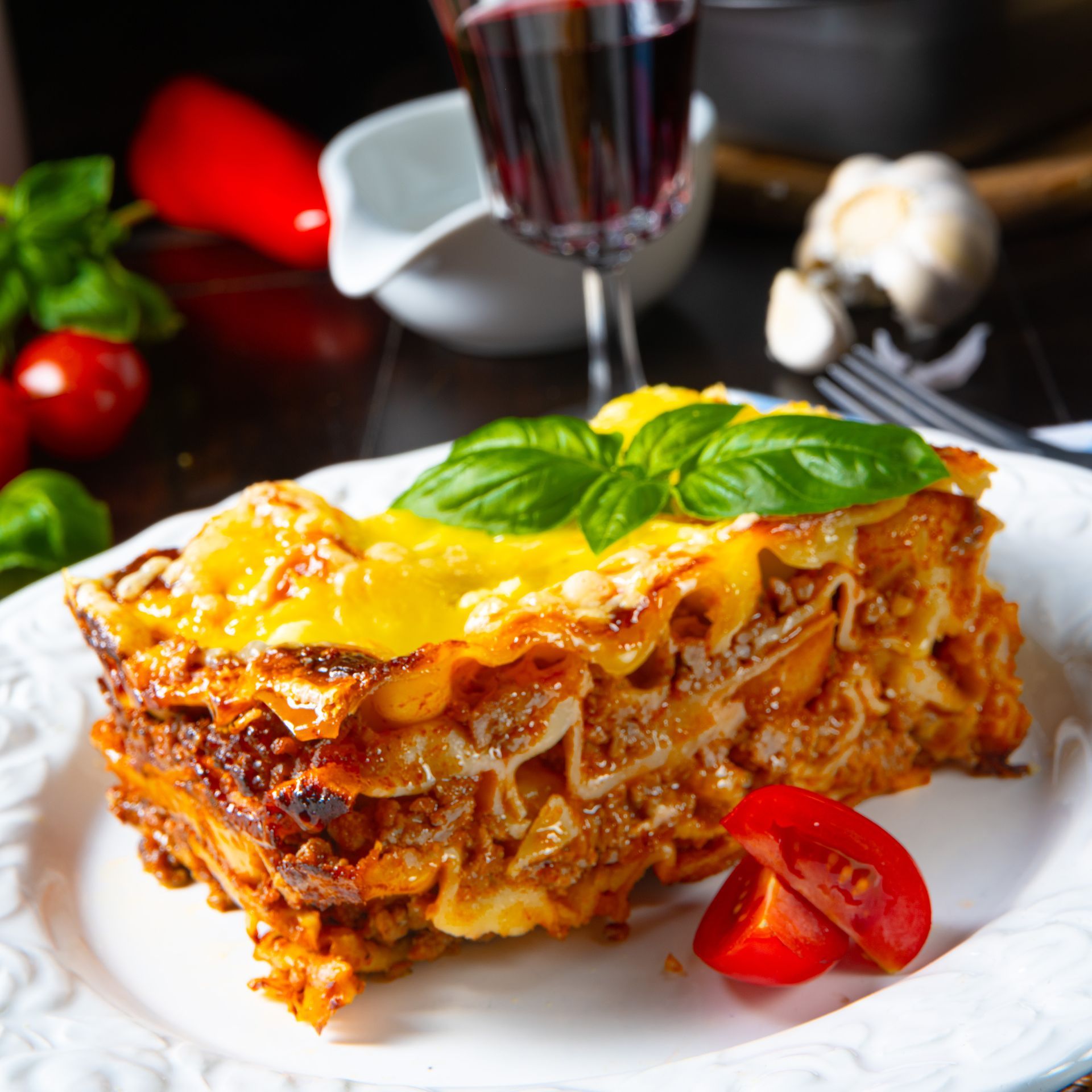 A slice of lasagna with tomatoes and basil on a white plate