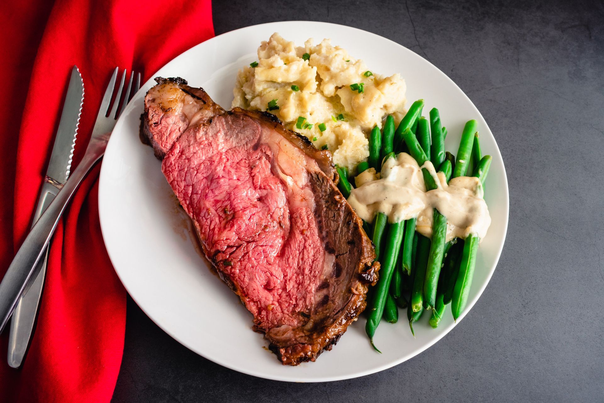 A white plate topped with a steak , mashed potatoes , green beans and gravy.