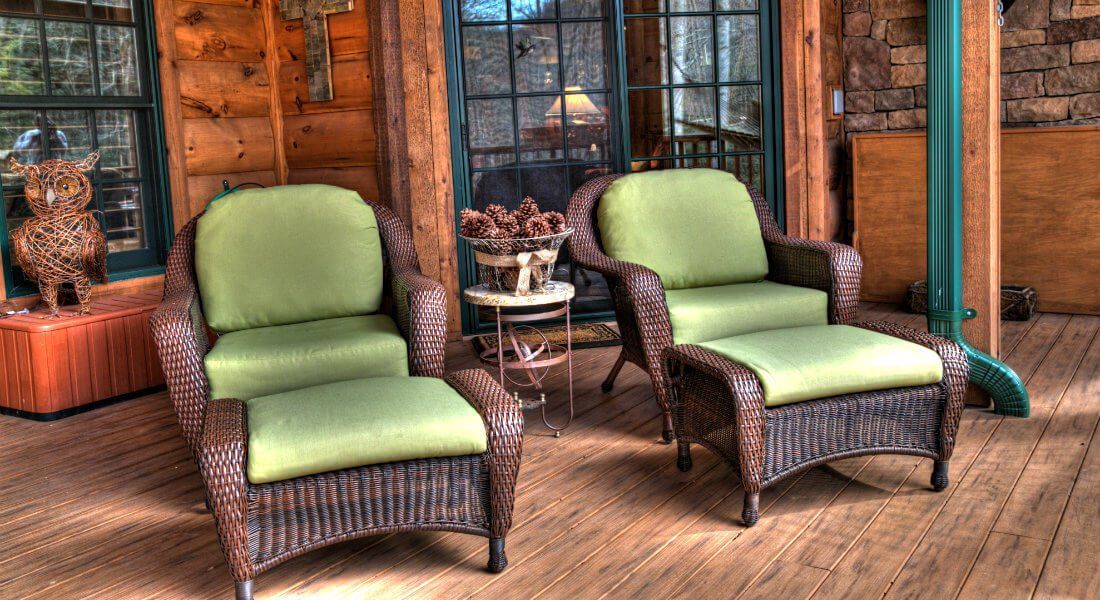 Two wicker chairs and ottomans are sitting on a wooden deck in front of a log cabin.