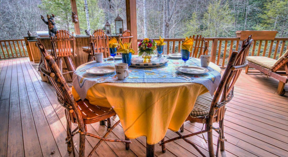 A table and chairs on a deck with a yellow table cloth.