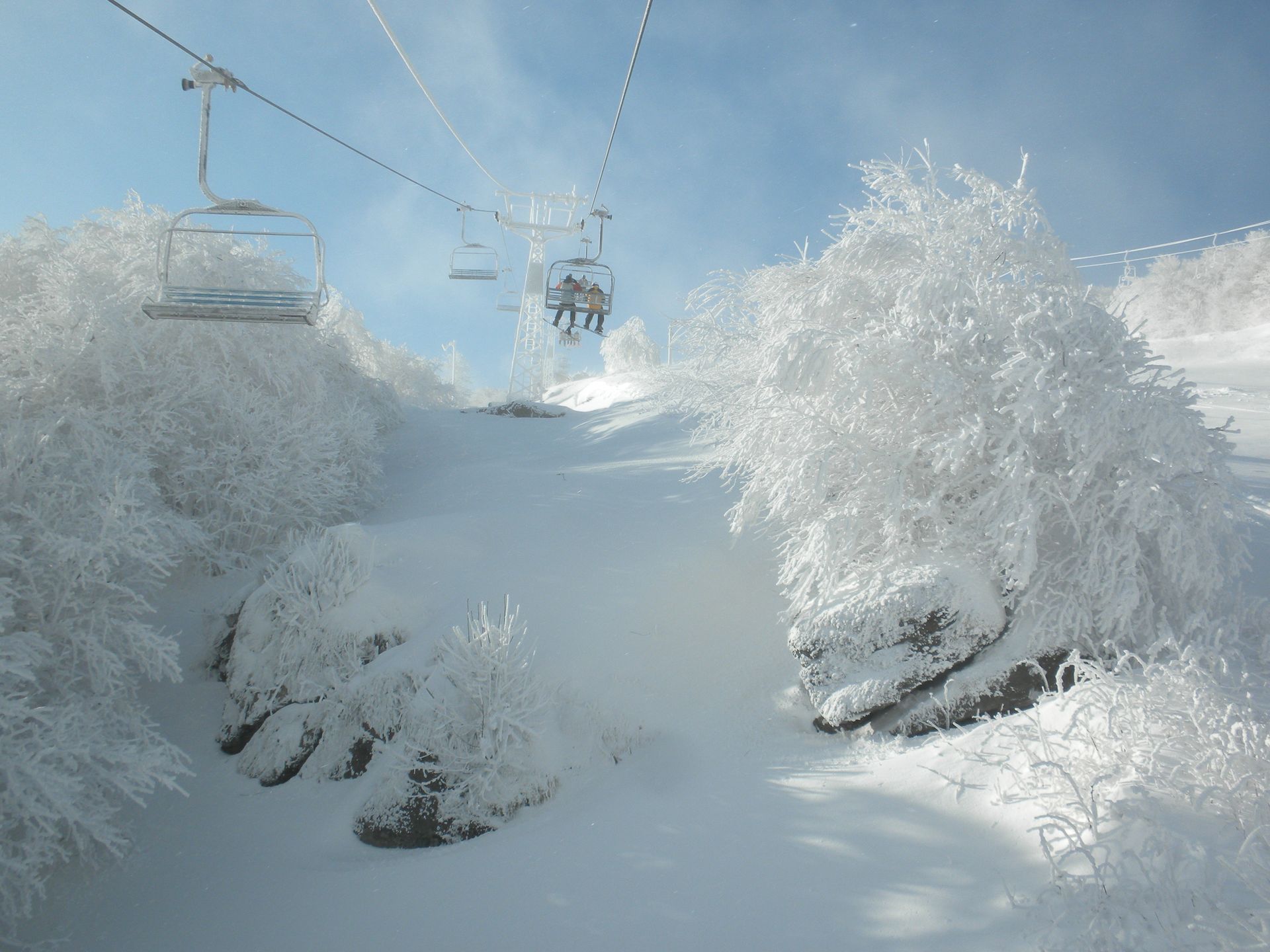 A ski lift is going down a snow covered slope.