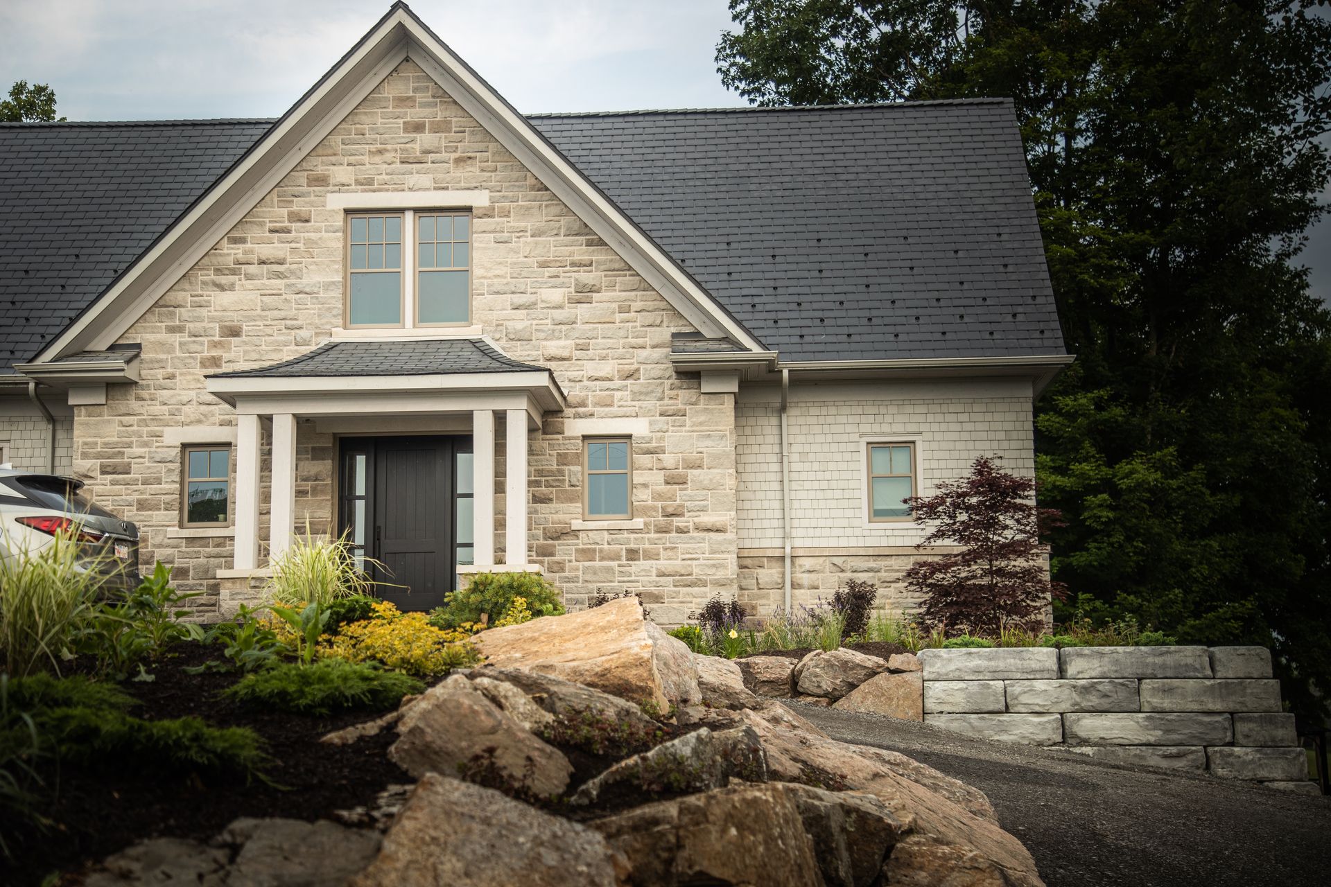Stone house with dark roof and trim, large rocks in foreground, landscaped yard.