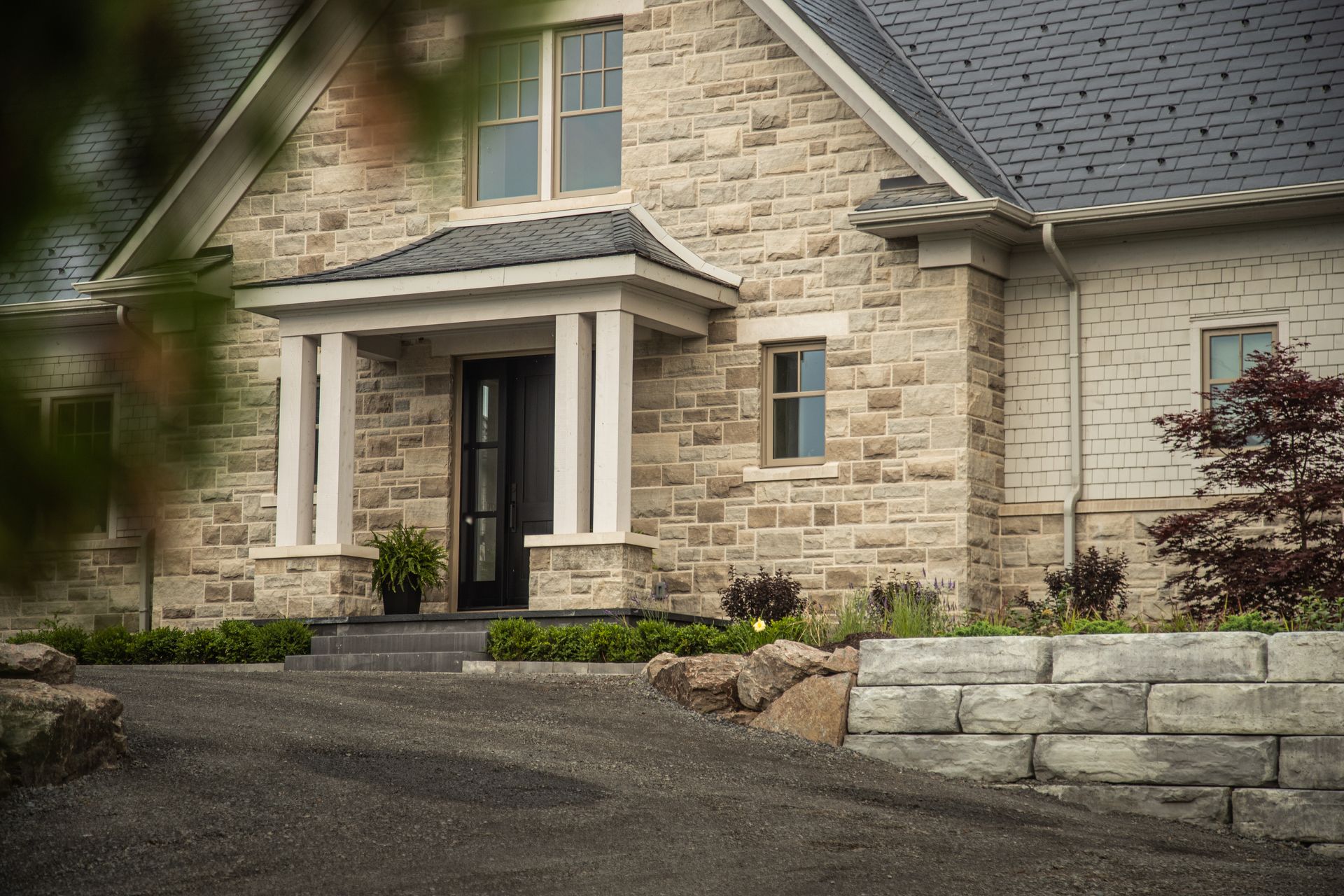 Stone house with covered entrance, dark door, and landscaped yard.