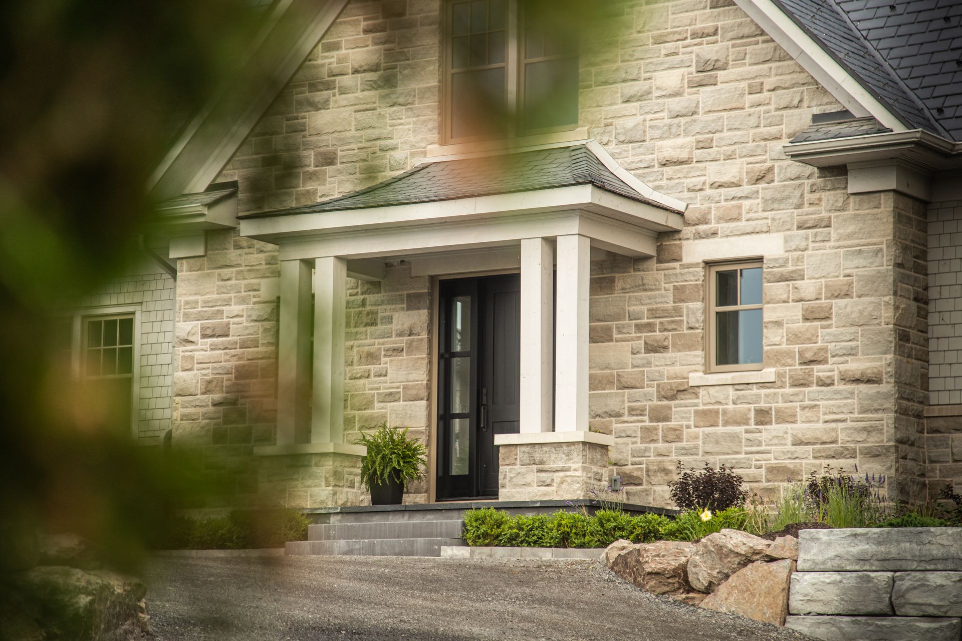 Stone house with covered entrance, black door, and gray roof.