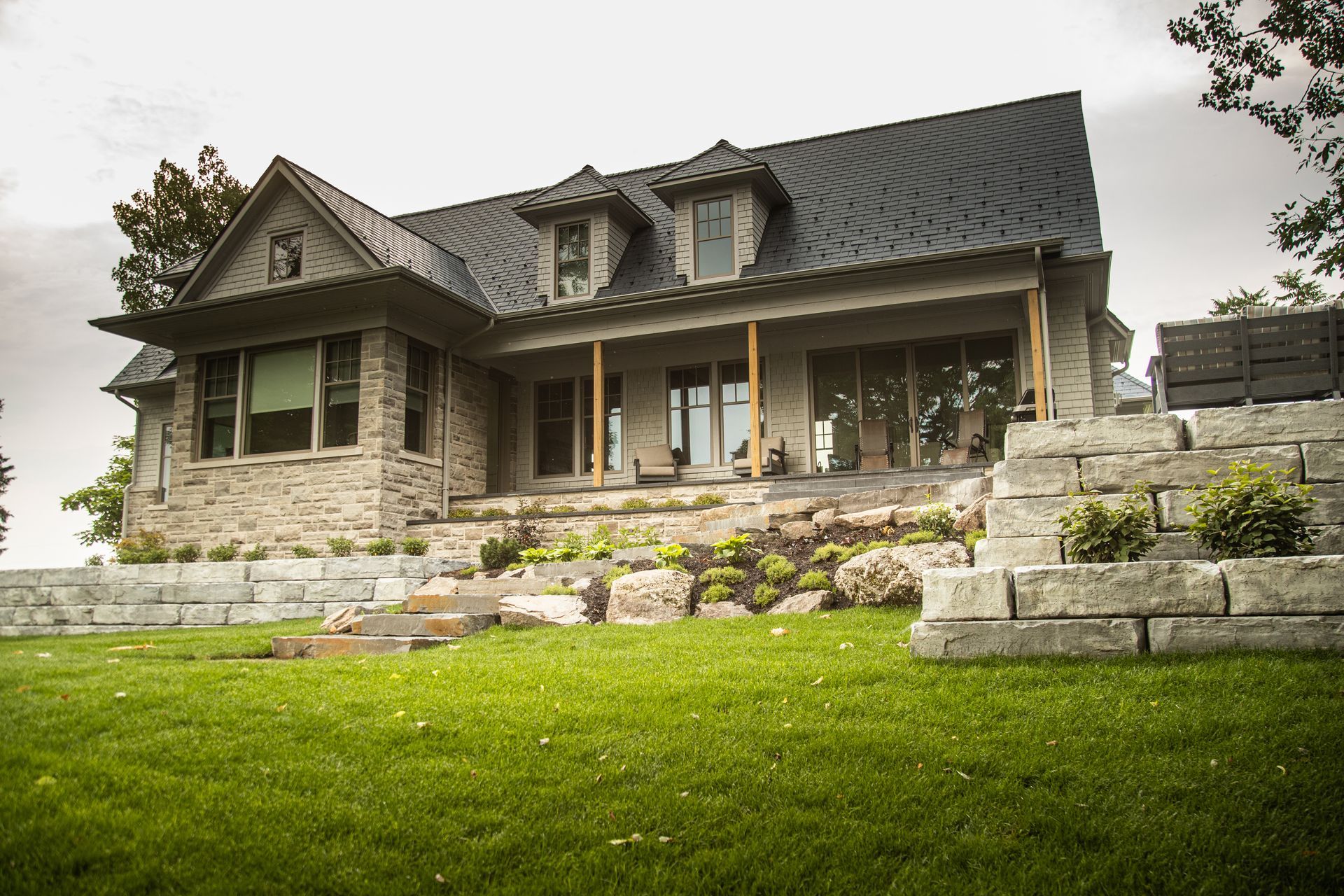 Stone house with black roof, covered porch, and landscaped yard.