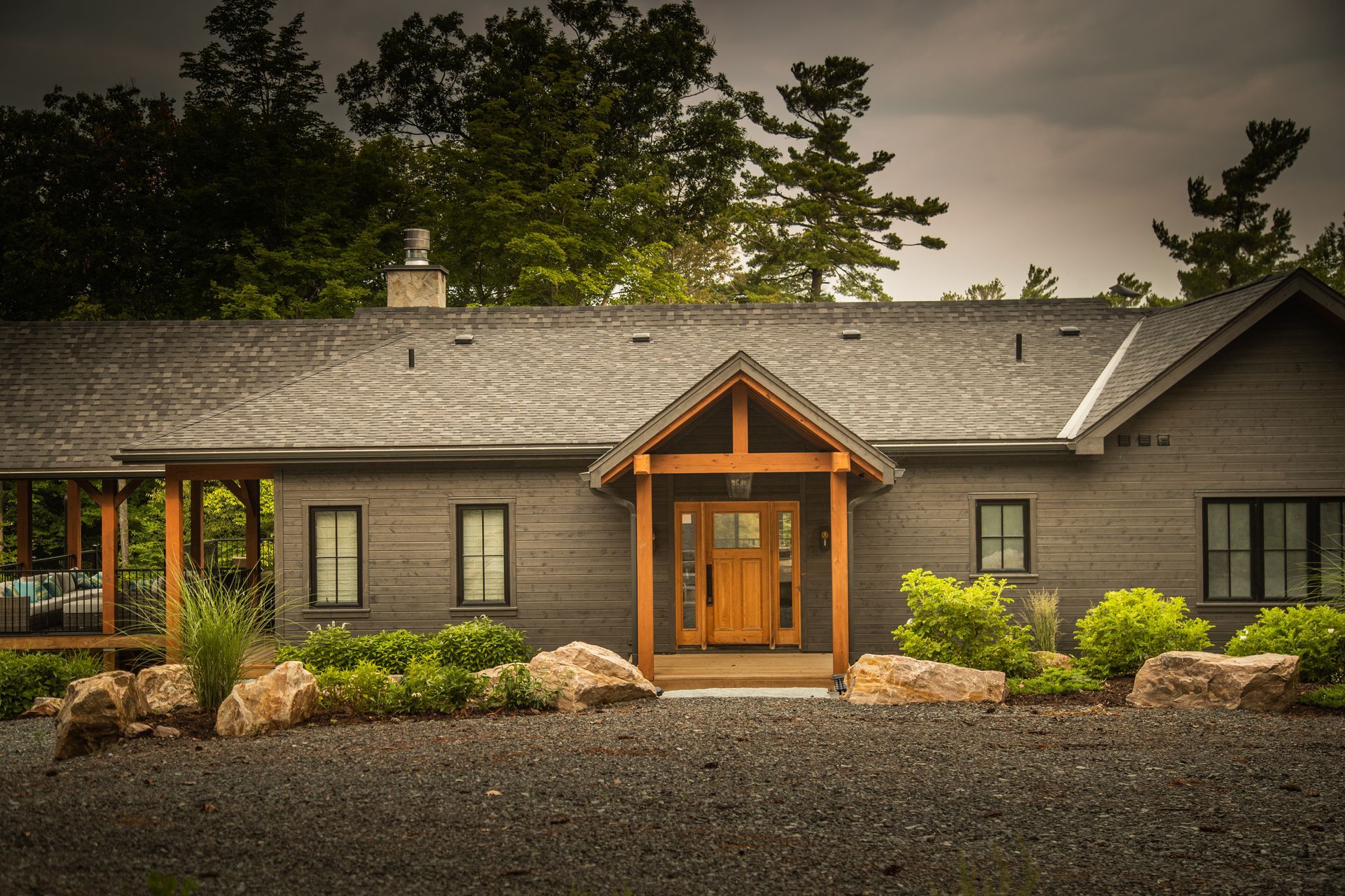 Gray house with wooden accents and brown door, surrounded by rocks and landscaping.