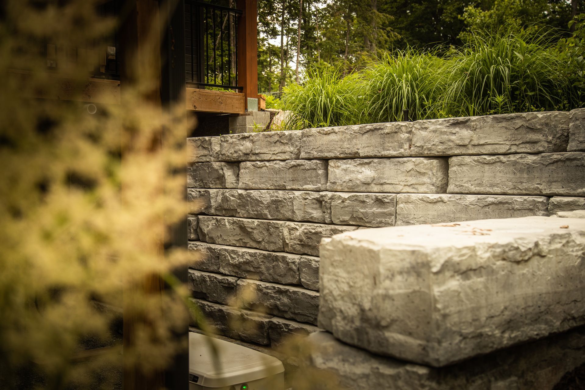 Stone retaining wall with a large block in the foreground and greenery behind.