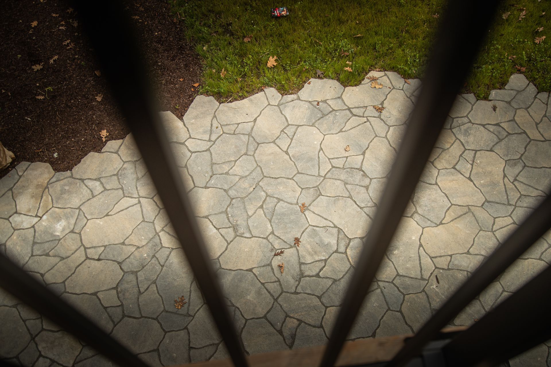 View from above a stone patio and grass, partially obscured by dark vertical bars.