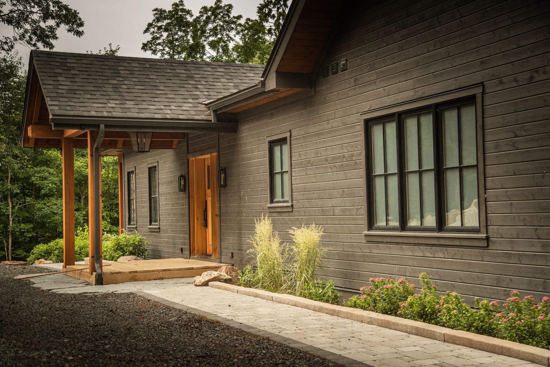 Gray brick home with wooden porch and dark-framed windows; walkway in front.