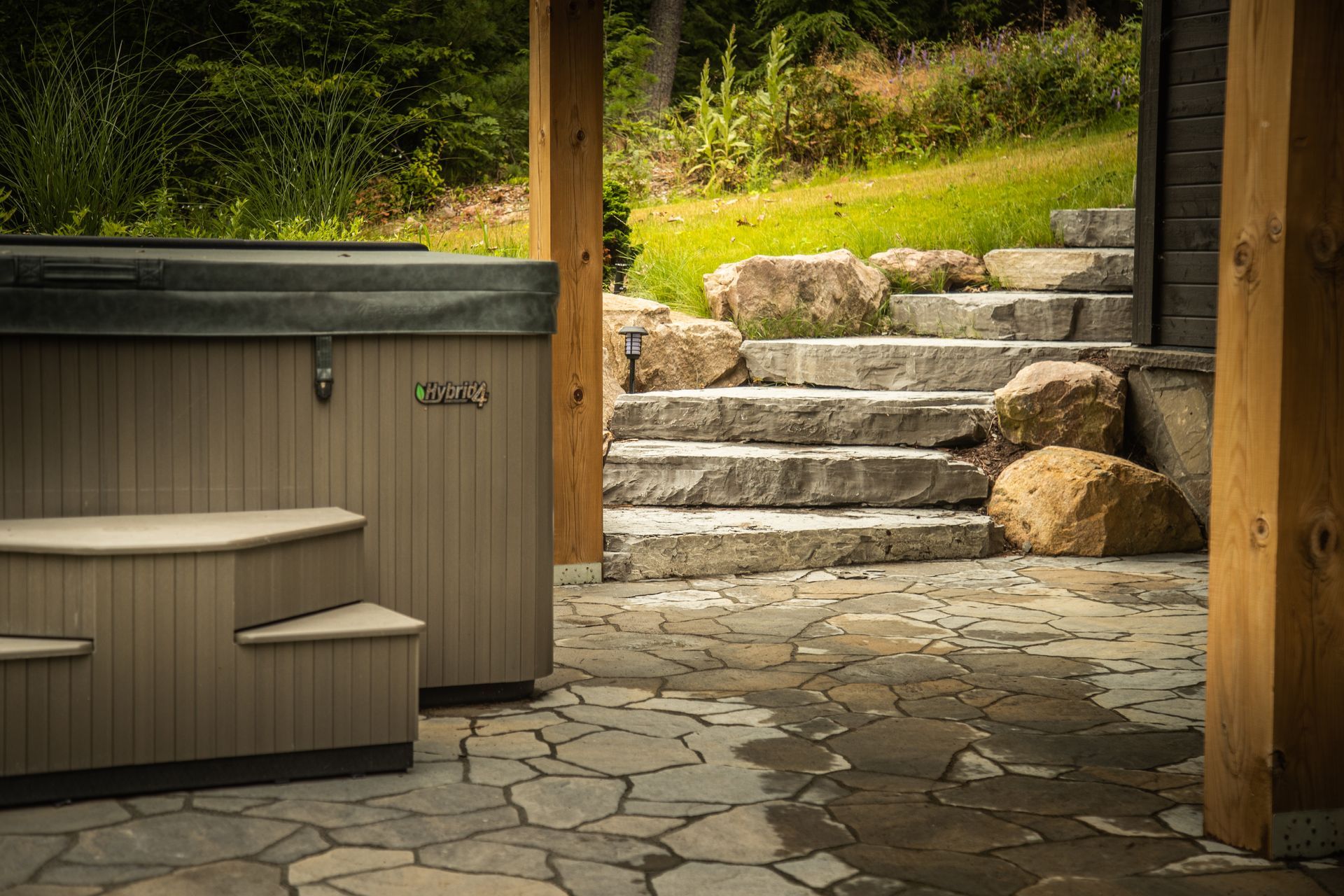 A hot tub with stairs sits next to stone stairs leading up a grassy hill.