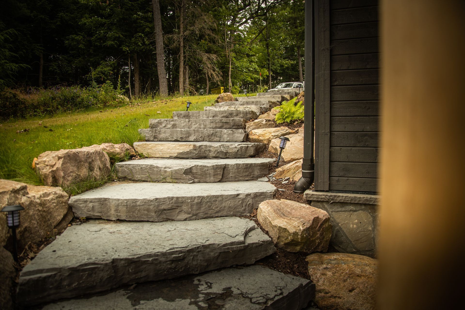 Stone steps leading up a grassy hill, flanked by rocks and a dark-sided building.