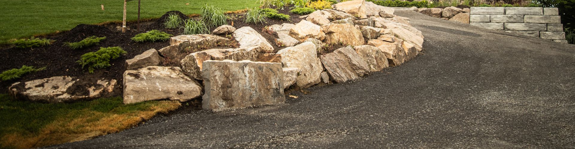 Natural stone retaining wall and landscaped garden bed along a paved driveway.