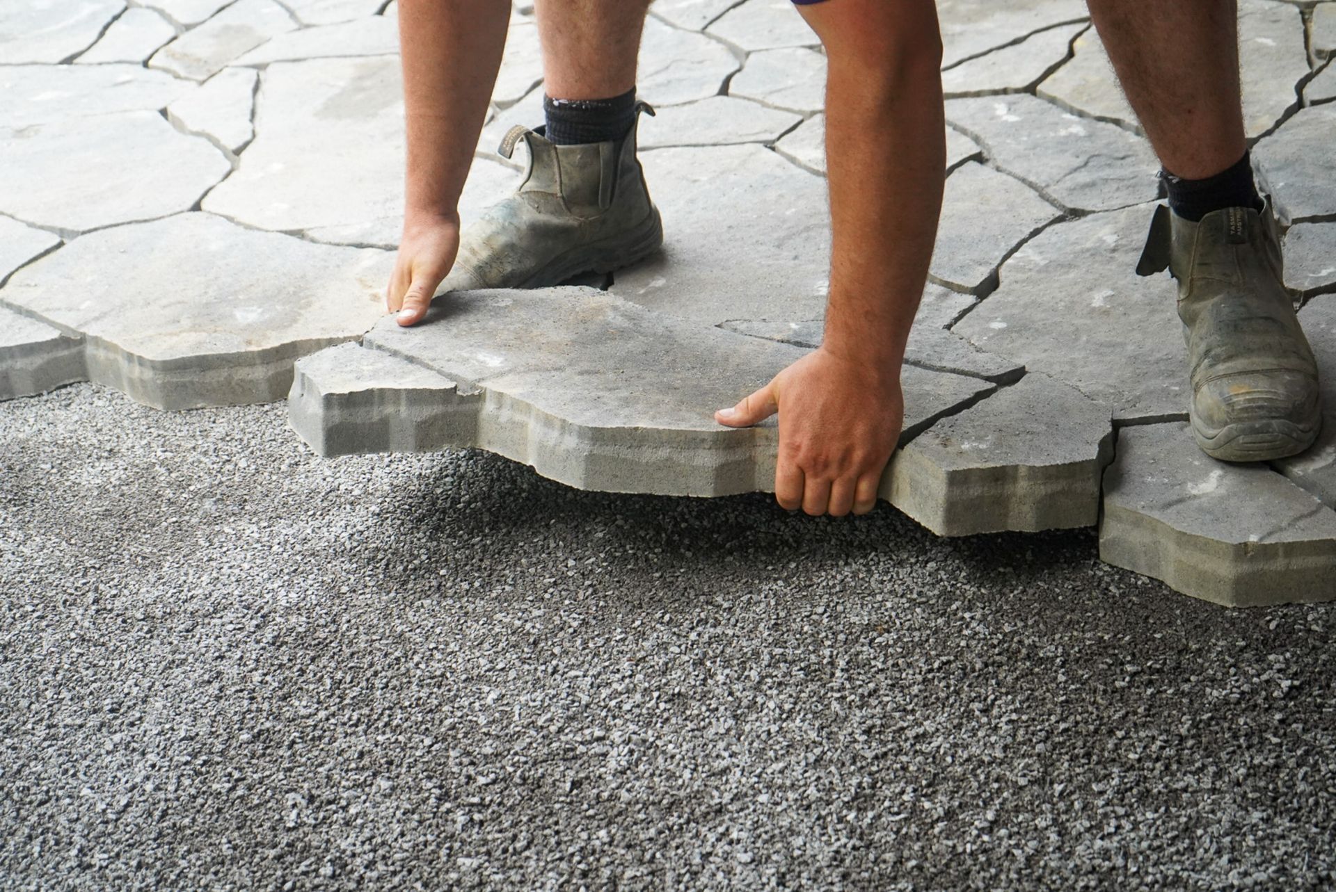 Person laying interlocking paving stones on gravel base.