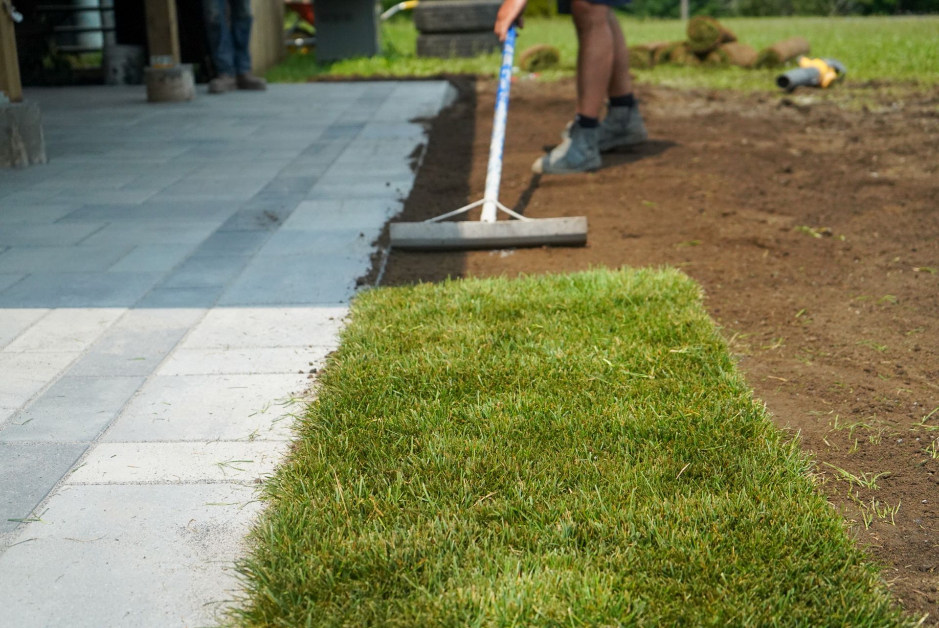 Laying sod next to a stone patio. A person uses a leveling tool on the dirt.