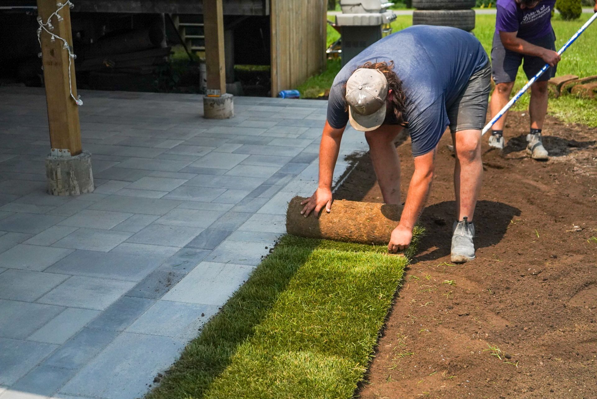 Man rolling out sod next to a stone patio. Another person stands nearby.