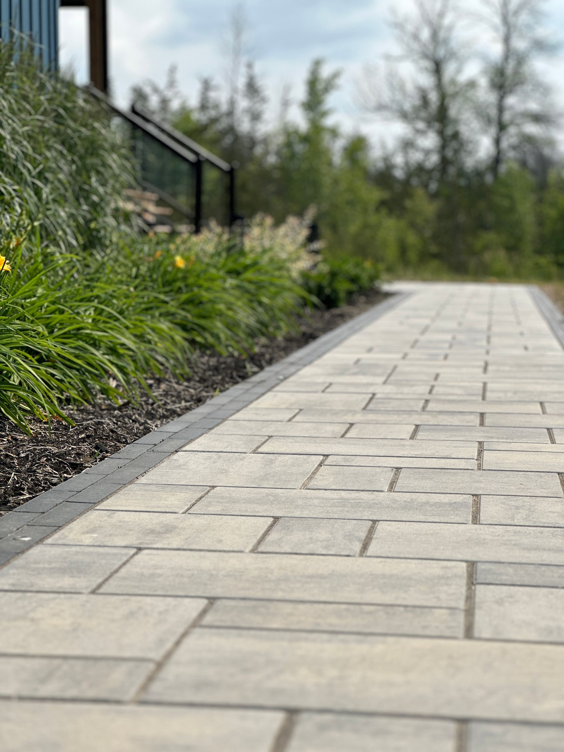 Stone path with a garden bed, leading towards a building in a natural setting.