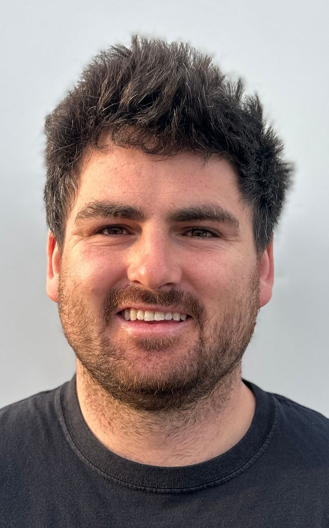 Smiling man with dark hair in a black shirt against a foggy backdrop.