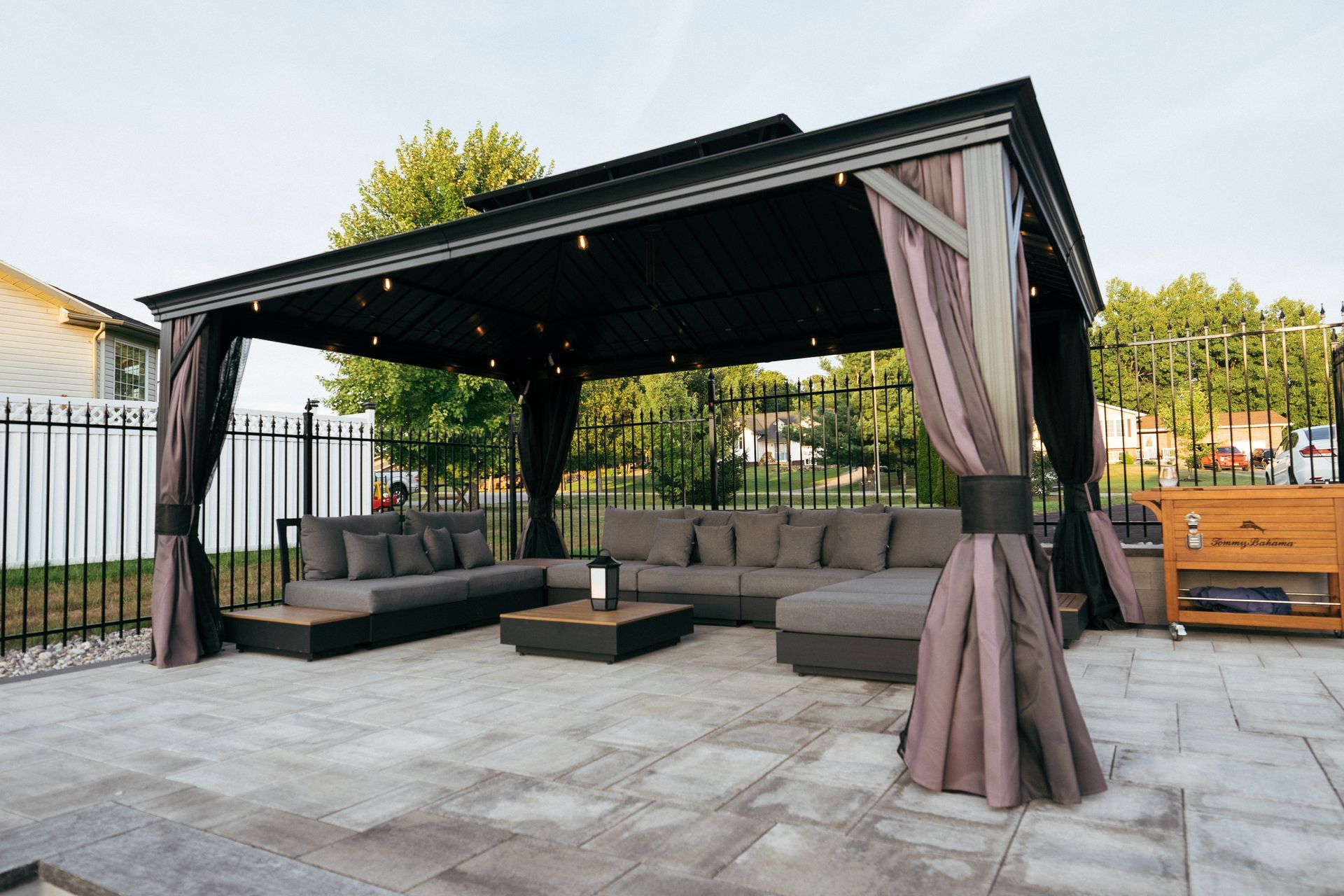 Gazebo with seating area on a stone patio, with curtains and string lights.