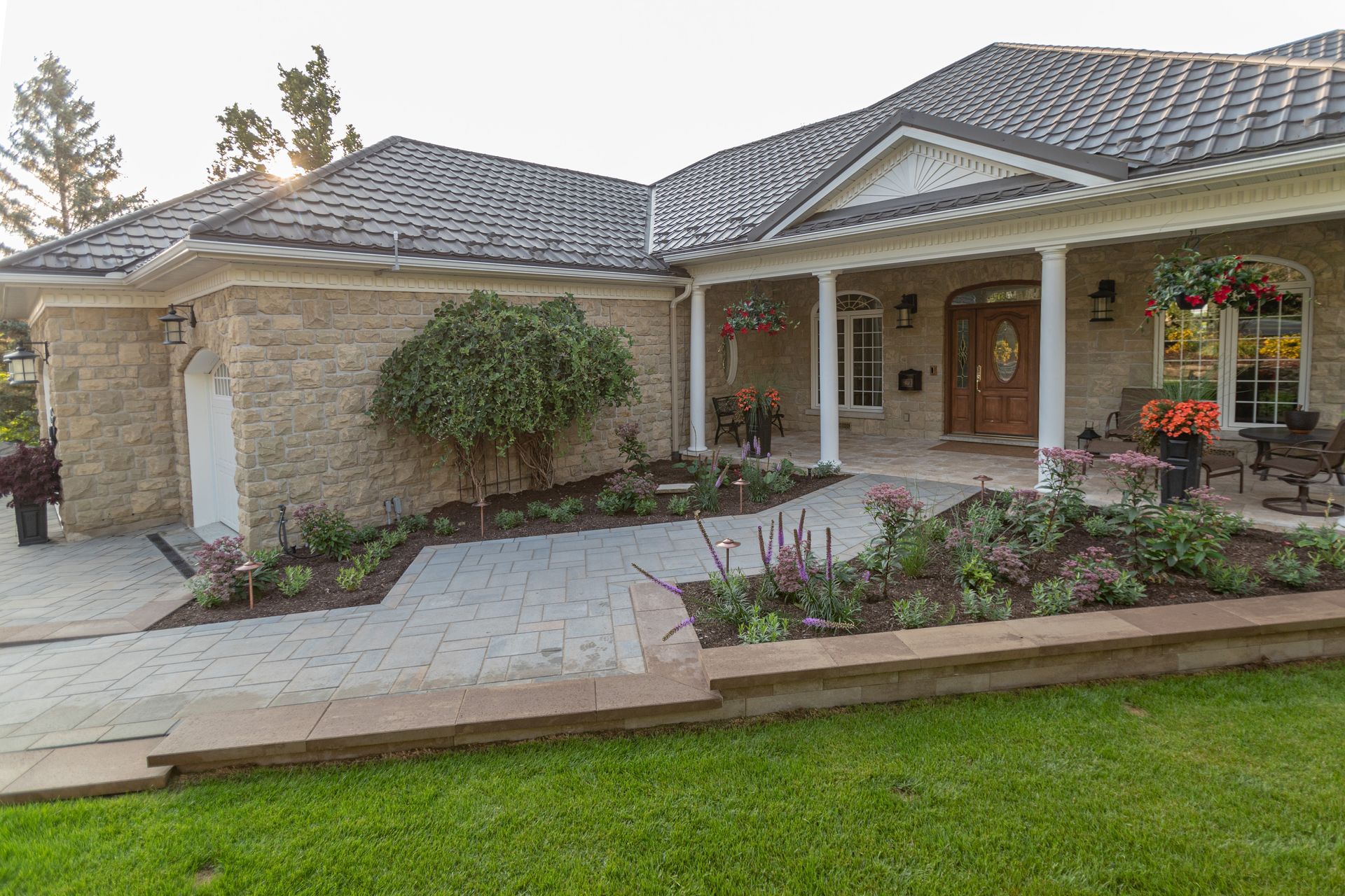 Exterior view of a stone house with a covered porch, surrounded by a landscaped yard and walkway.