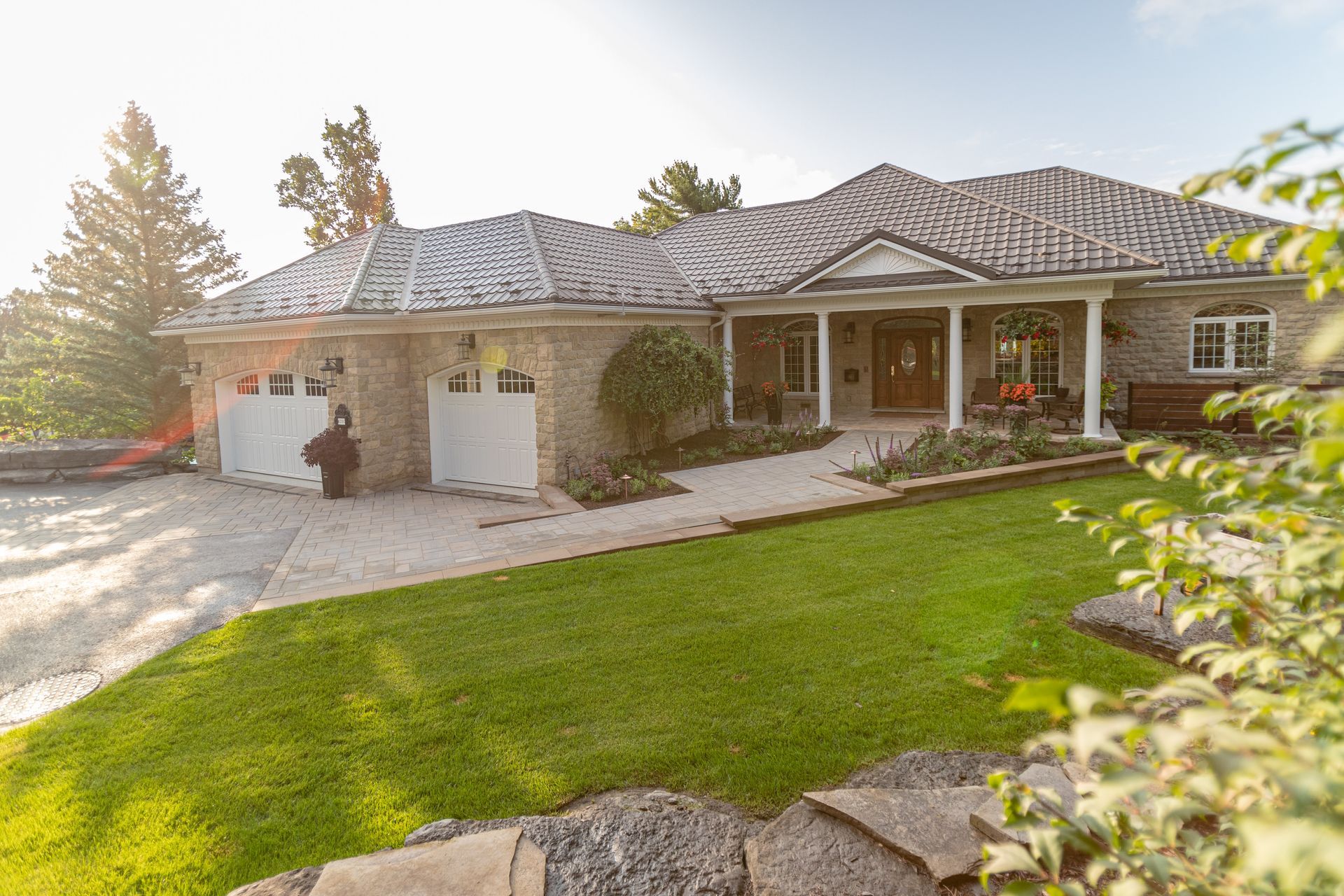 Stone house with a two-car garage, porch, and well-manicured lawn on a sunny day.