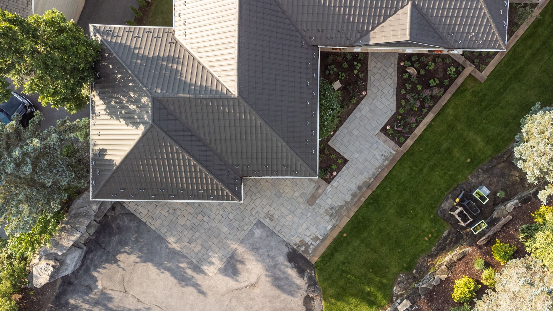 Overhead view of house with dark gray roof, paved driveway and walkway, and green lawn.