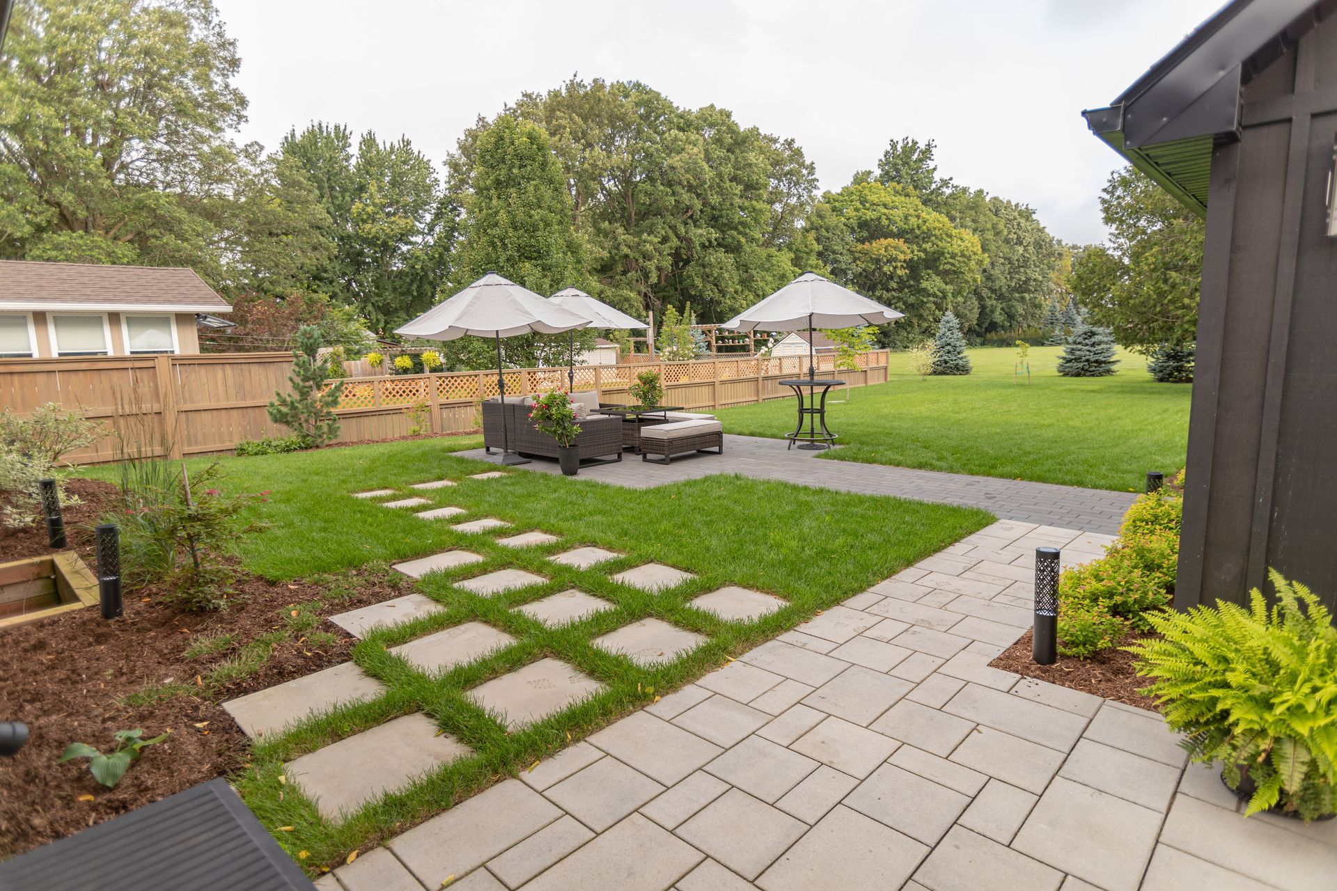 Backyard patio with paved pathway, lounge seating, umbrellas, and lawn.