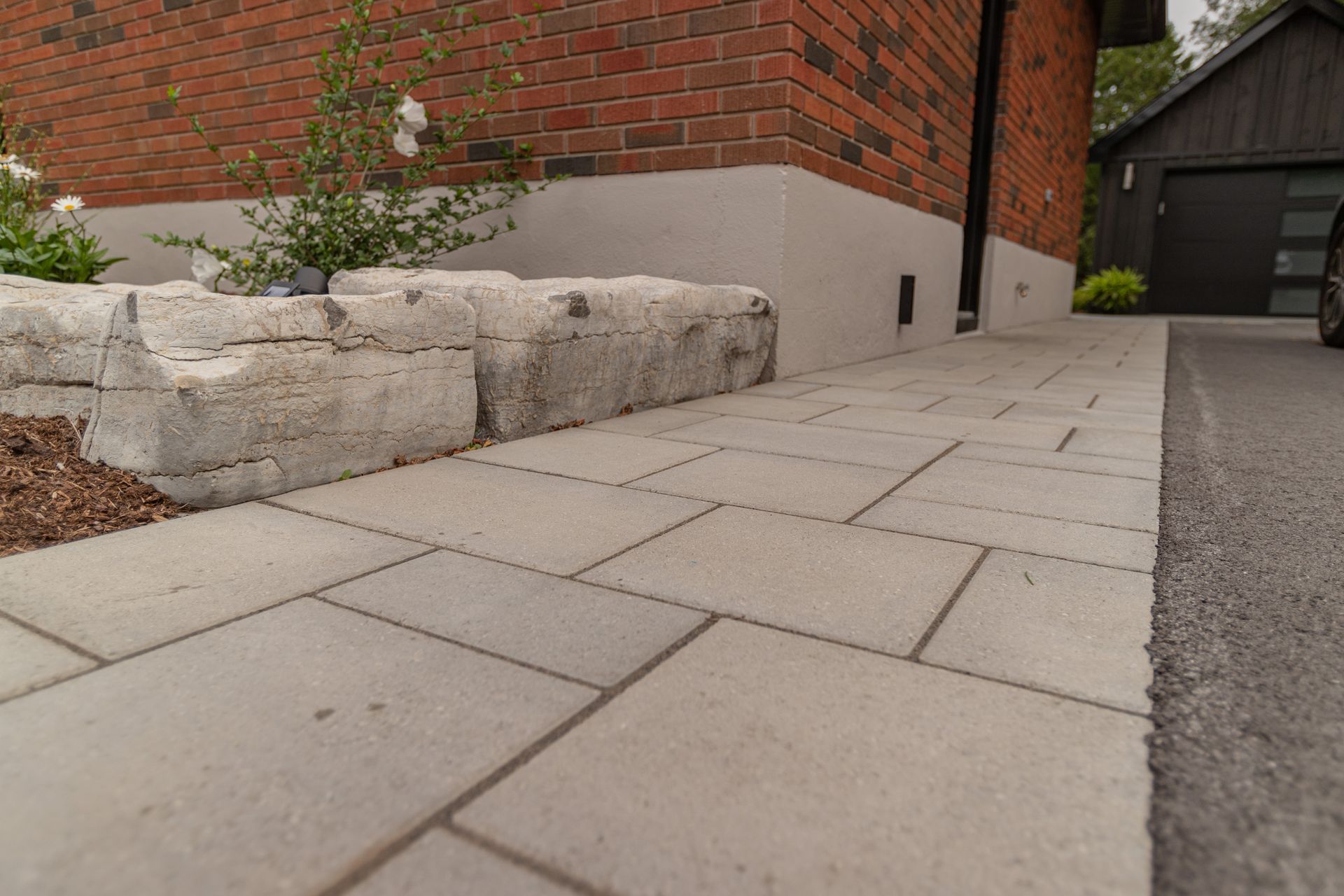 Brick house exterior with a paved walkway bordered by stone blocks and a driveway.