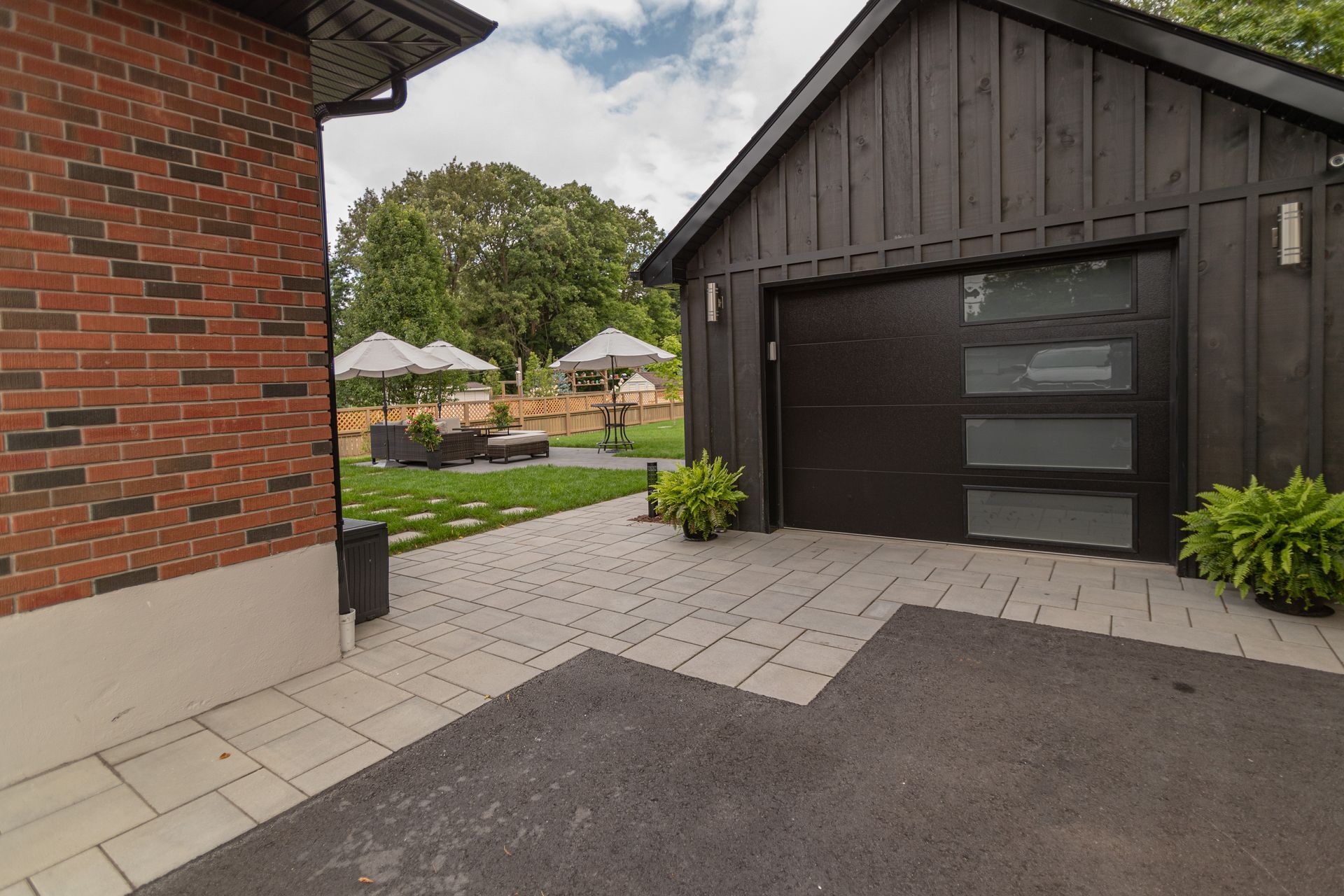 Black garage with glass panel door next to a brick building; patio and lawn with umbrellas visible.