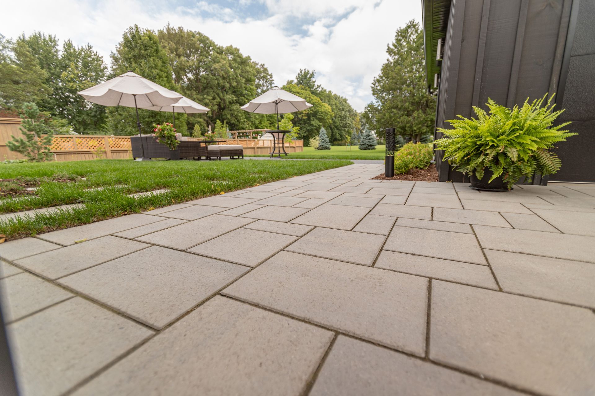 Gray stone patio leading to lawn with patio furniture and umbrellas.